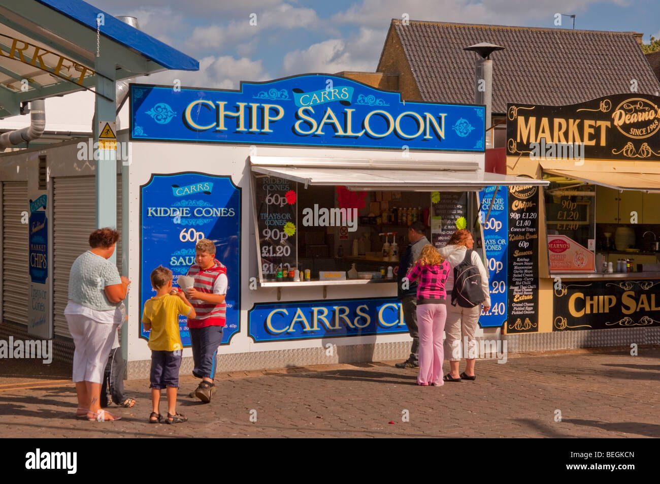 Persone mangiare patatine da un chip in stallo ( la Carrs chip berlina ) al mercato di Great Yarmouth , Norfolk , Regno Unito Foto Stock