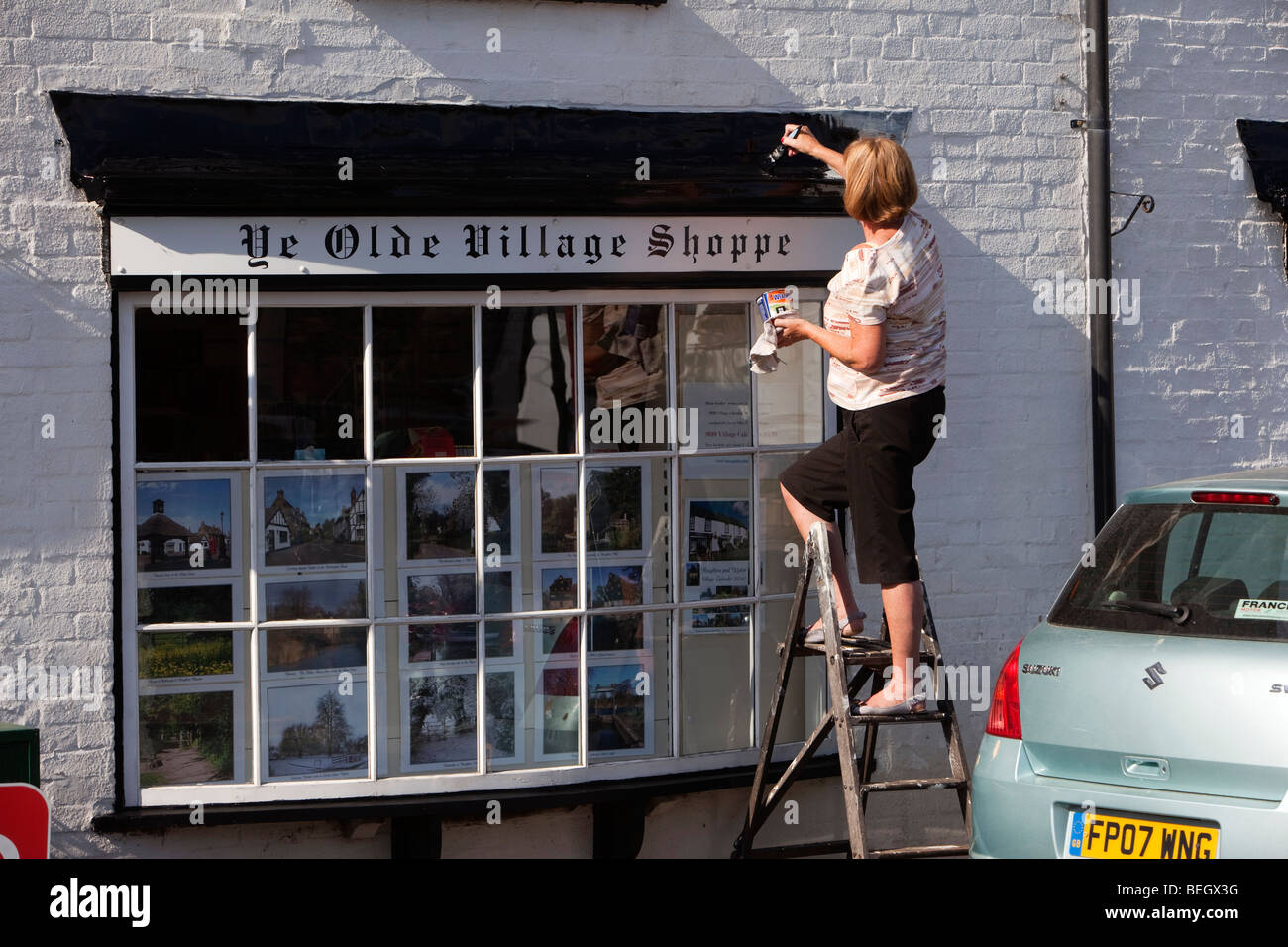 Inghilterra, Cambridgeshire, Huntingdon, Houghton negozio del villaggio, donna su scala dipinto sul telaio di una finestra Foto Stock