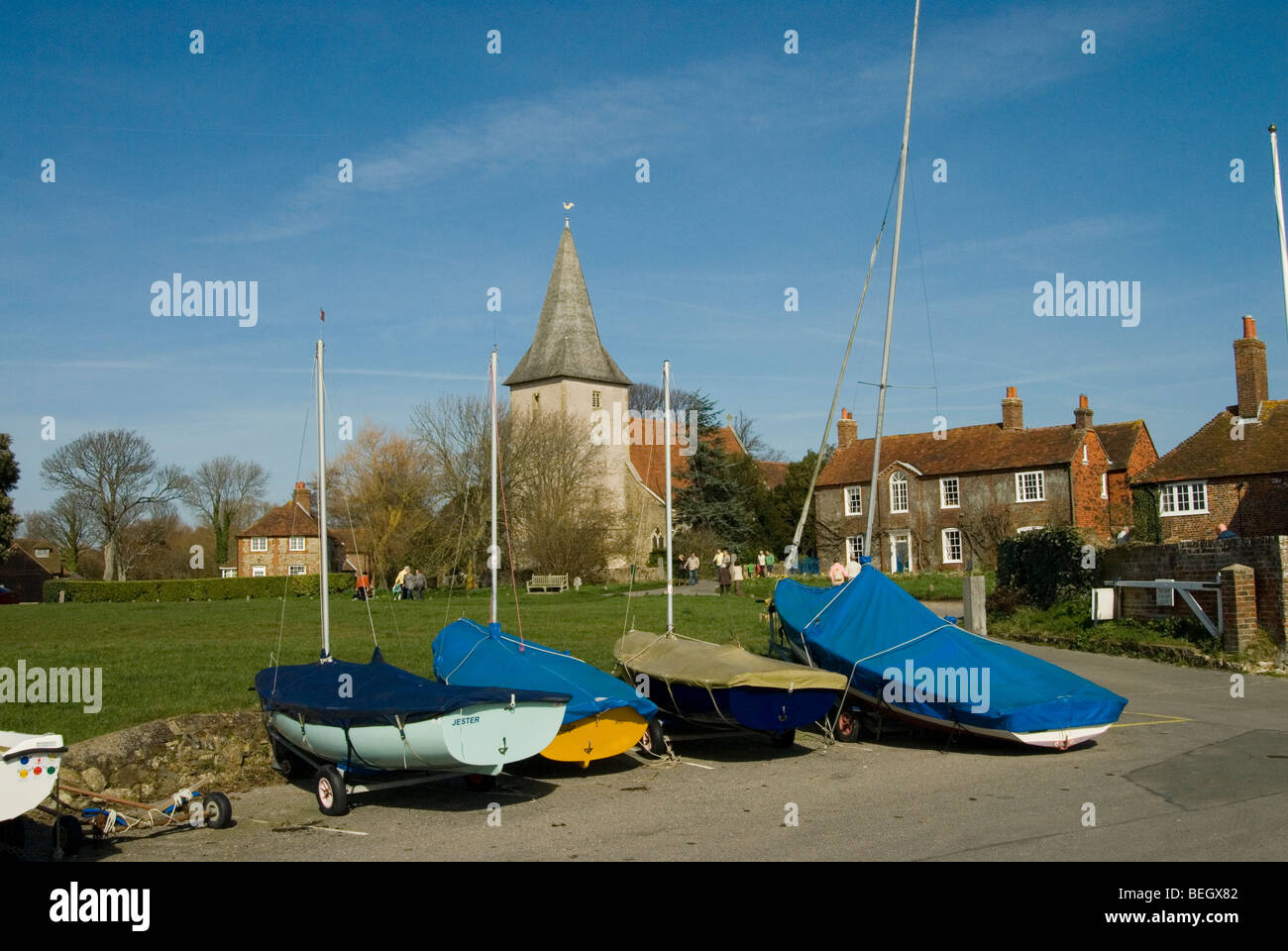 Chiesa di Bosham con quattro barche con copertine su situato di fronte ad esso in una bella giornata con cielo blu chiaro Foto Stock