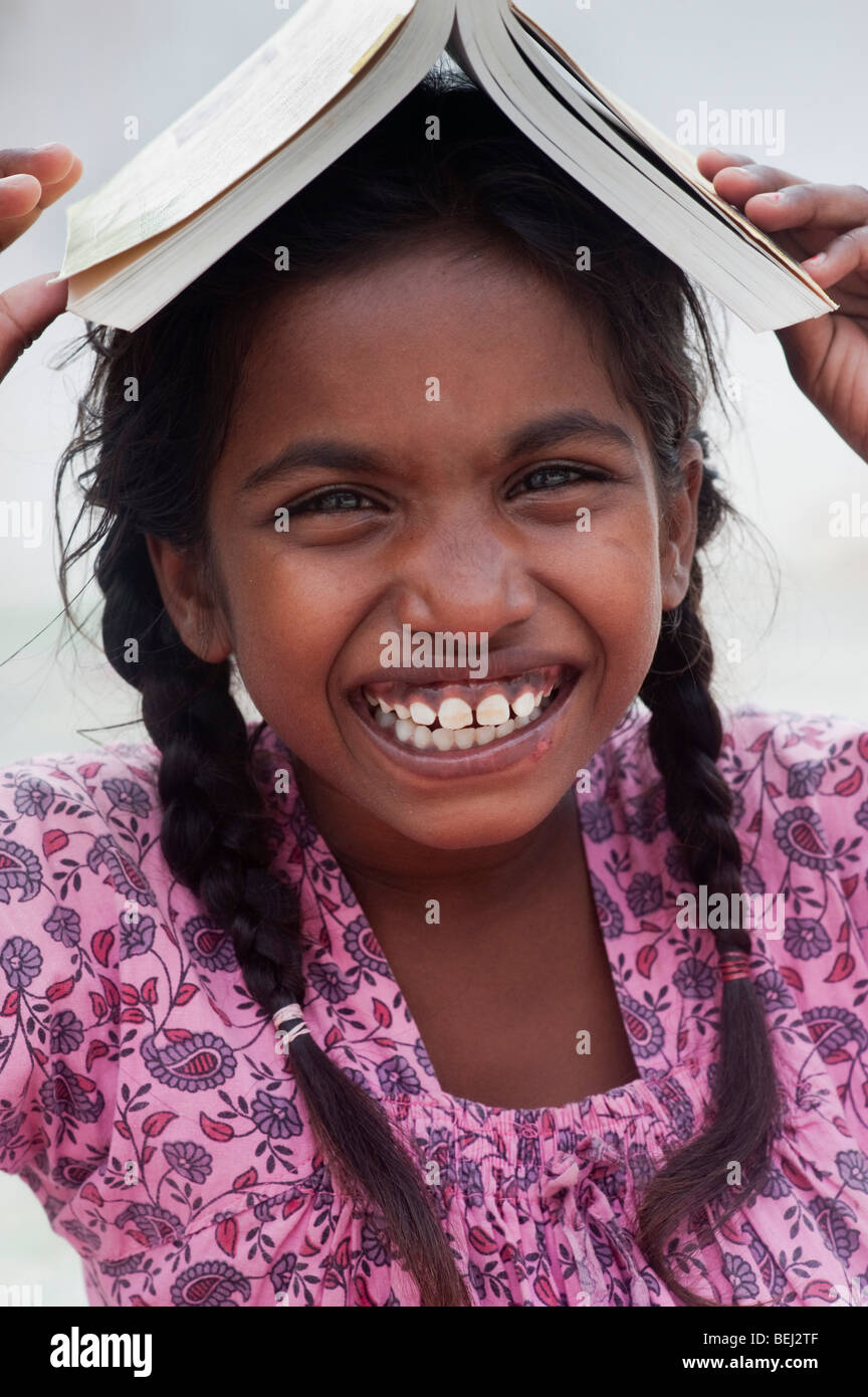 Bella ragazza indiana felicemente sorridente con un libro sulla sua testa Foto Stock