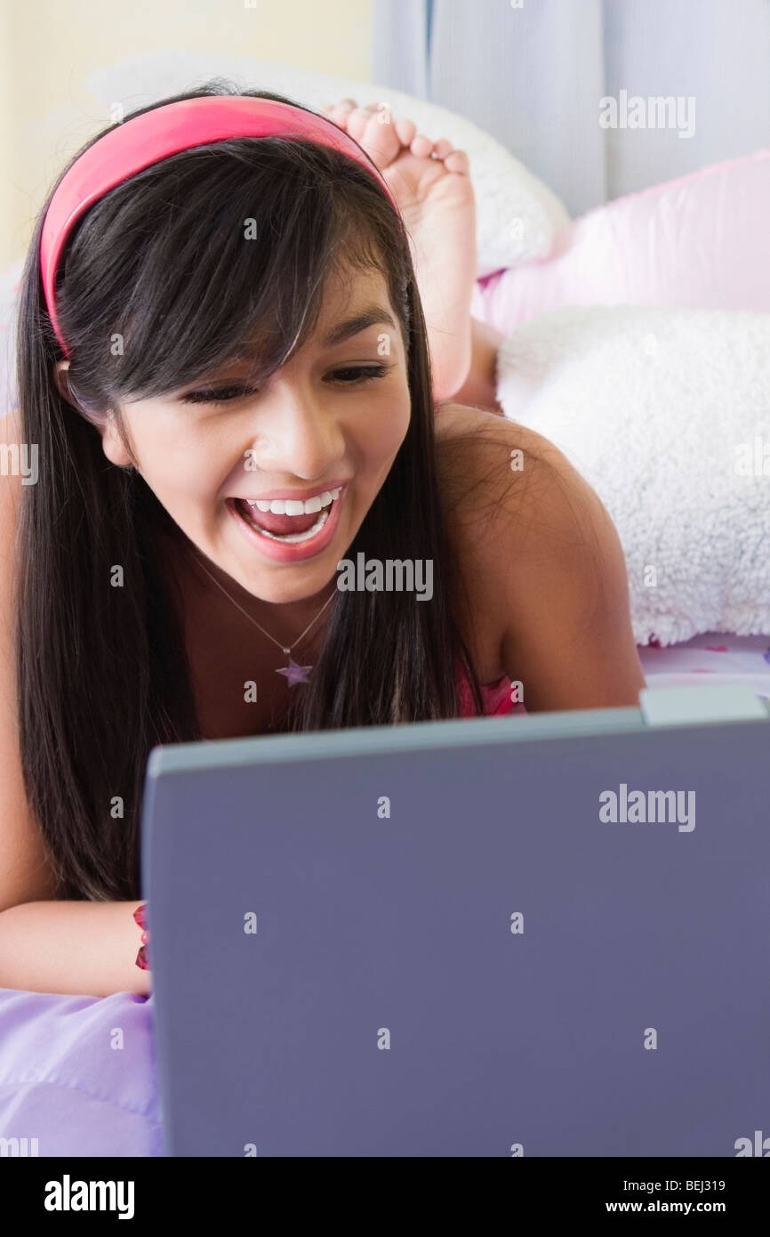 Close-up di una ragazza adolescente giacente sul letto e al lavoro su un notebook Foto Stock