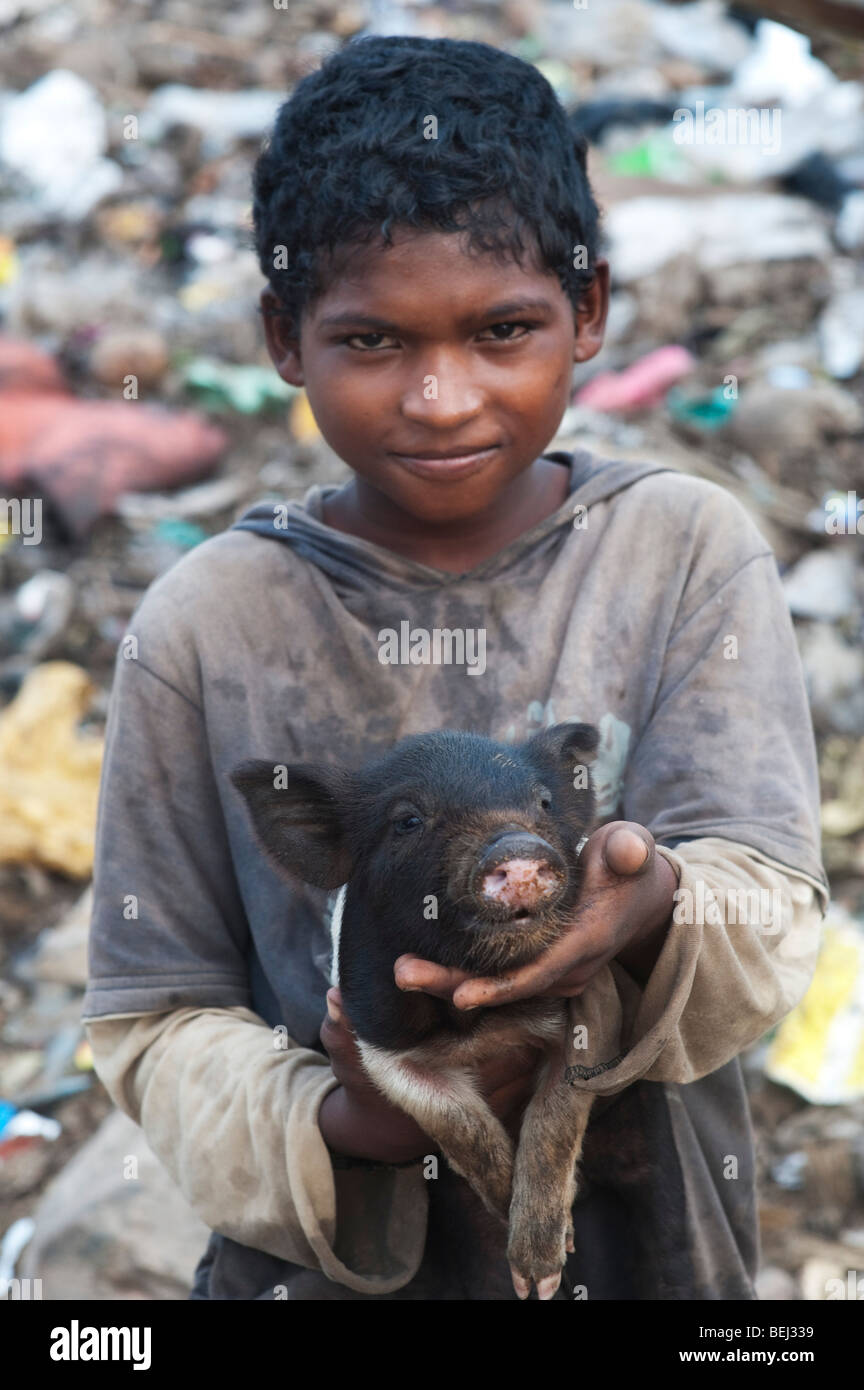Casta inferiore ragazzo indiano con piccole maiale in una discarica. Andhra Pradesh, India Foto Stock