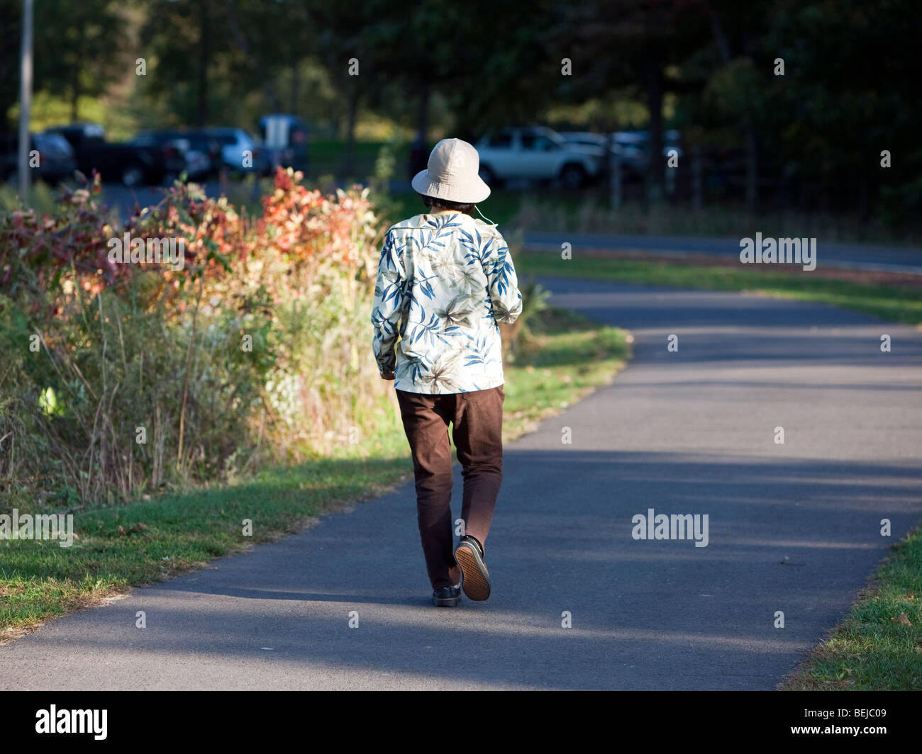 Una donna che indossa un morbido floppy hat e una maglietta fiorito passeggiate nel parco. Foto Stock