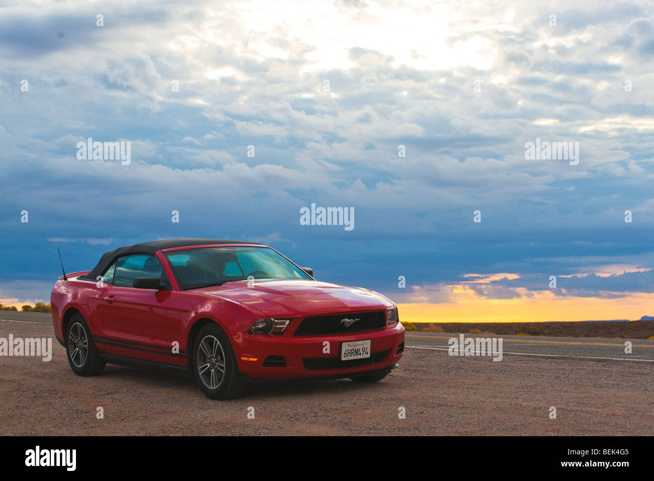 Red Ford Mustang cabriolet da una strada nel deserto contro il cielo drammatico in Arizona, southwesternUSA. Foto Stock