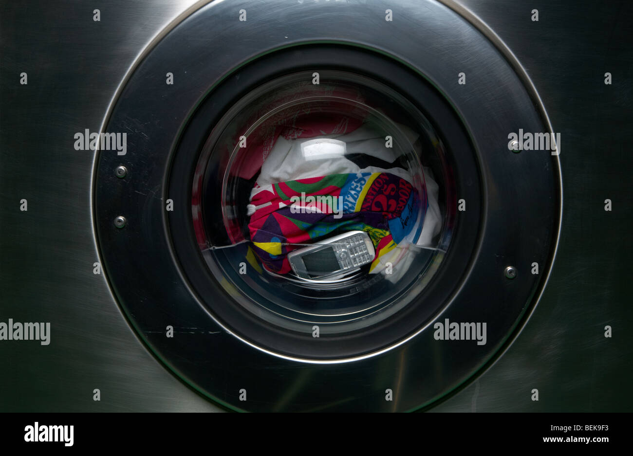 Un telefono cellulare si siede in una macchina di lavaggio con un pieno carico di panni. Foto Stock