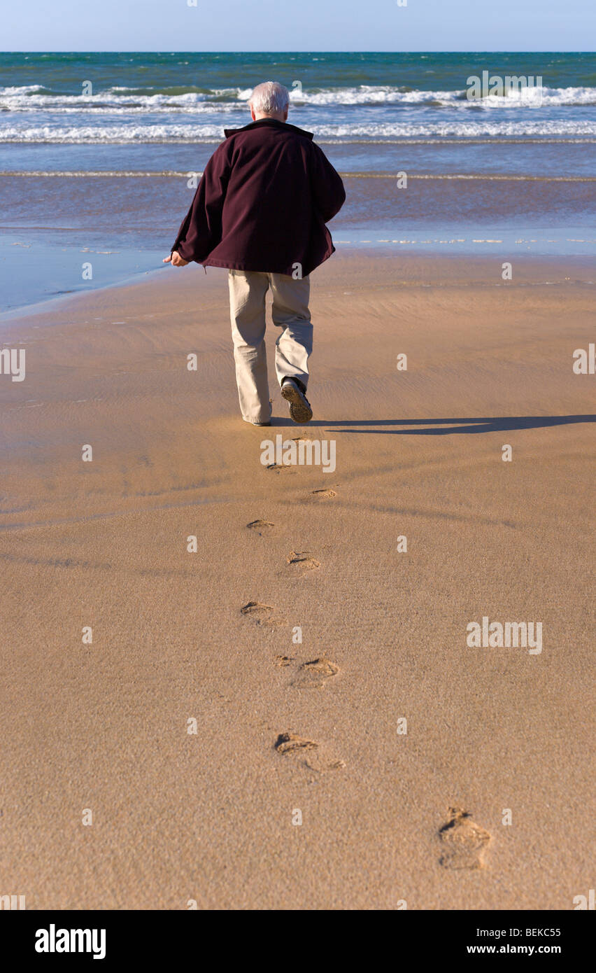 Uomo a camminare sulla spiaggia verso il mare Foto Stock