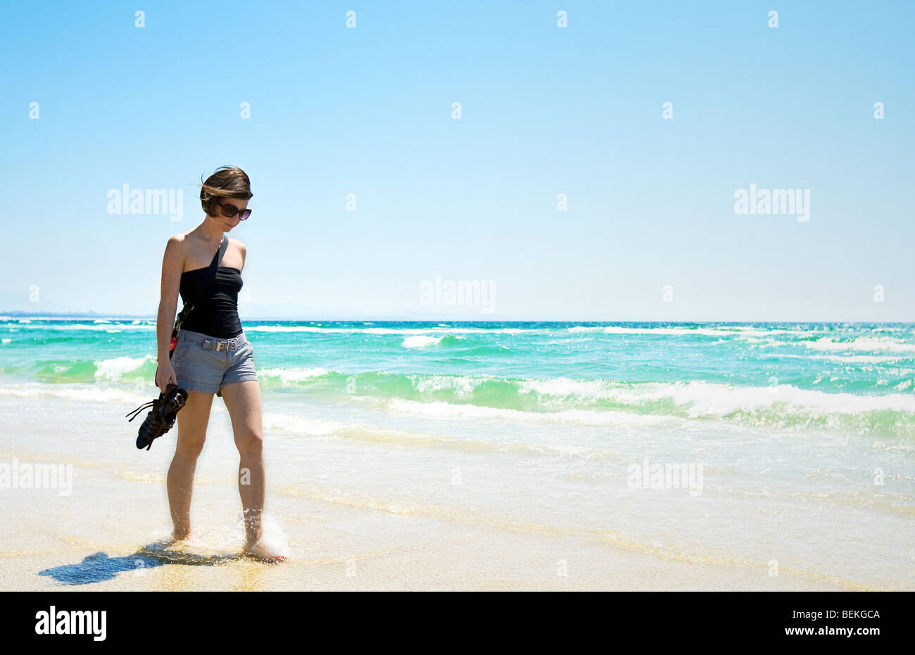Colpo di un attraente Brunette camminando lungo un assolato Beach Foto Stock