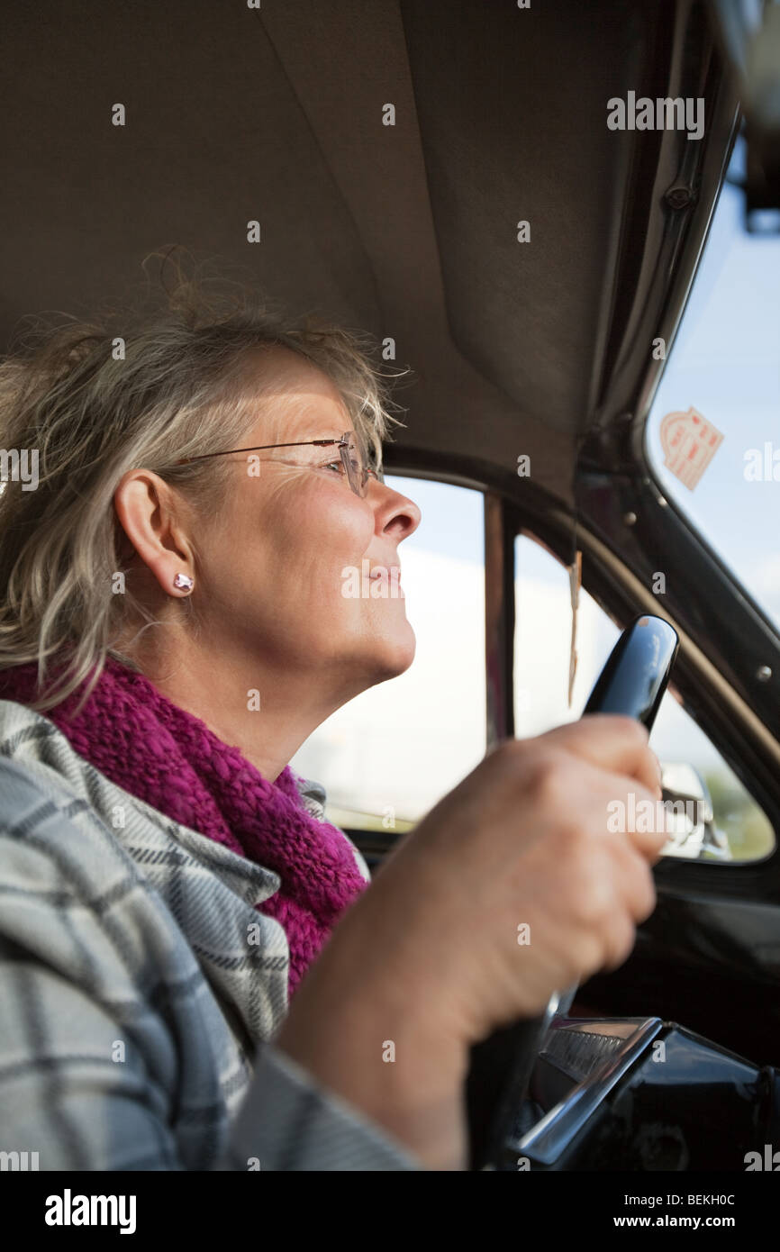 Felice senior donna alla guida di un'auto oldtimer Foto Stock