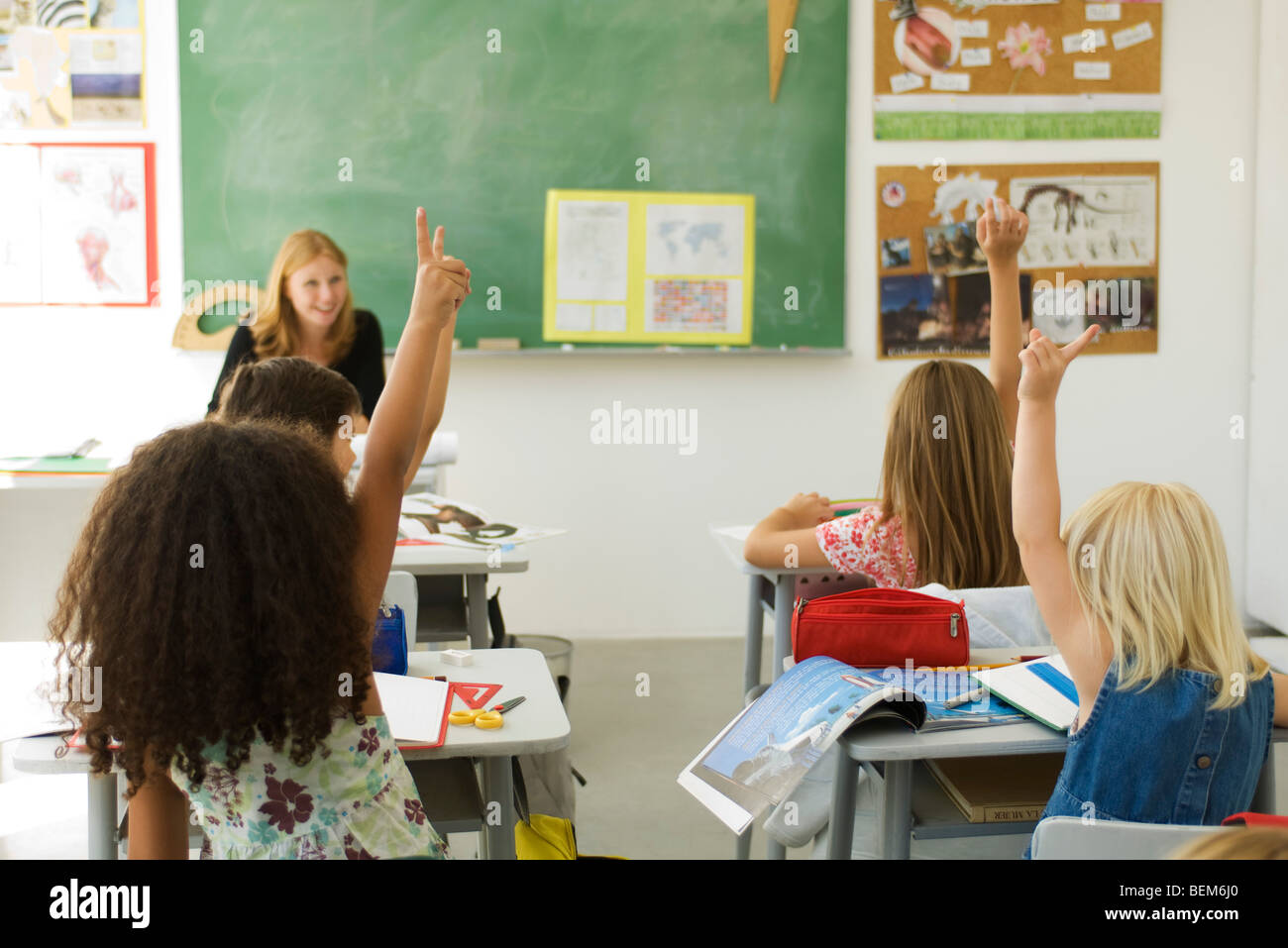 Gli studenti elementari in aula alzando le mani, vista posteriore Foto Stock