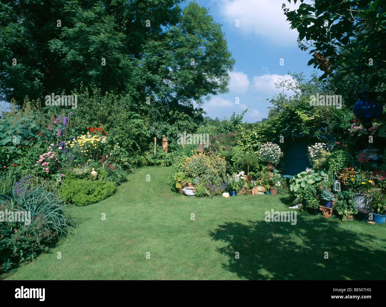 Piante fiorite in bordi intorno a prato in paese giardino in estate Foto Stock