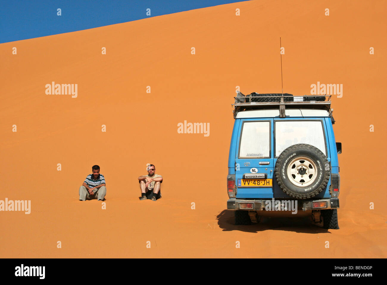Turistico con guida seduta accanto al veicolo a quattro ruote motrici sulla sabbia rossa a Duna Erg Chebbi, il deserto del Sahara, Marocco, Africa del Nord Foto Stock