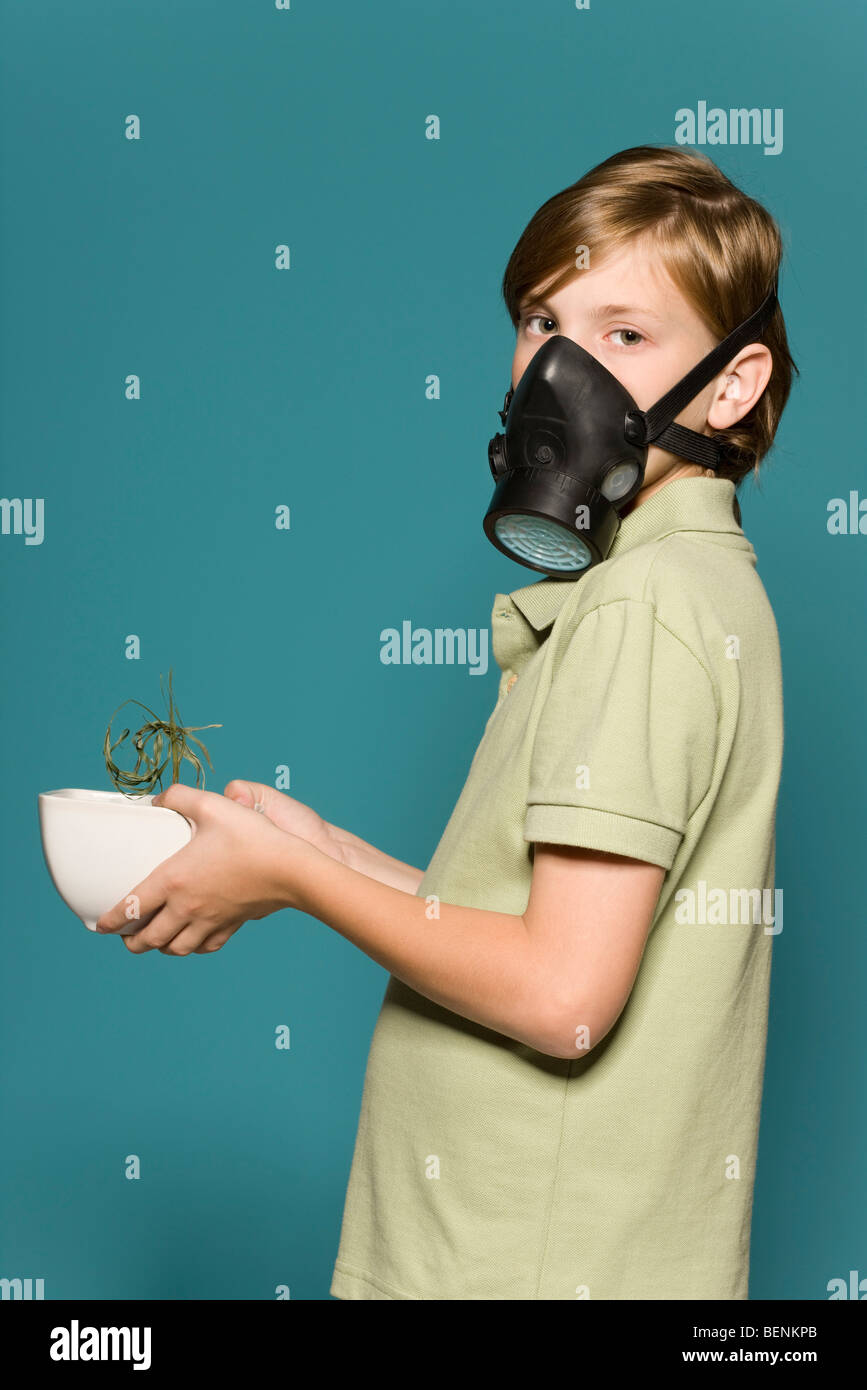 Ragazzo che indossa maschera a gas, tenendo appassì pianta in vaso Foto Stock