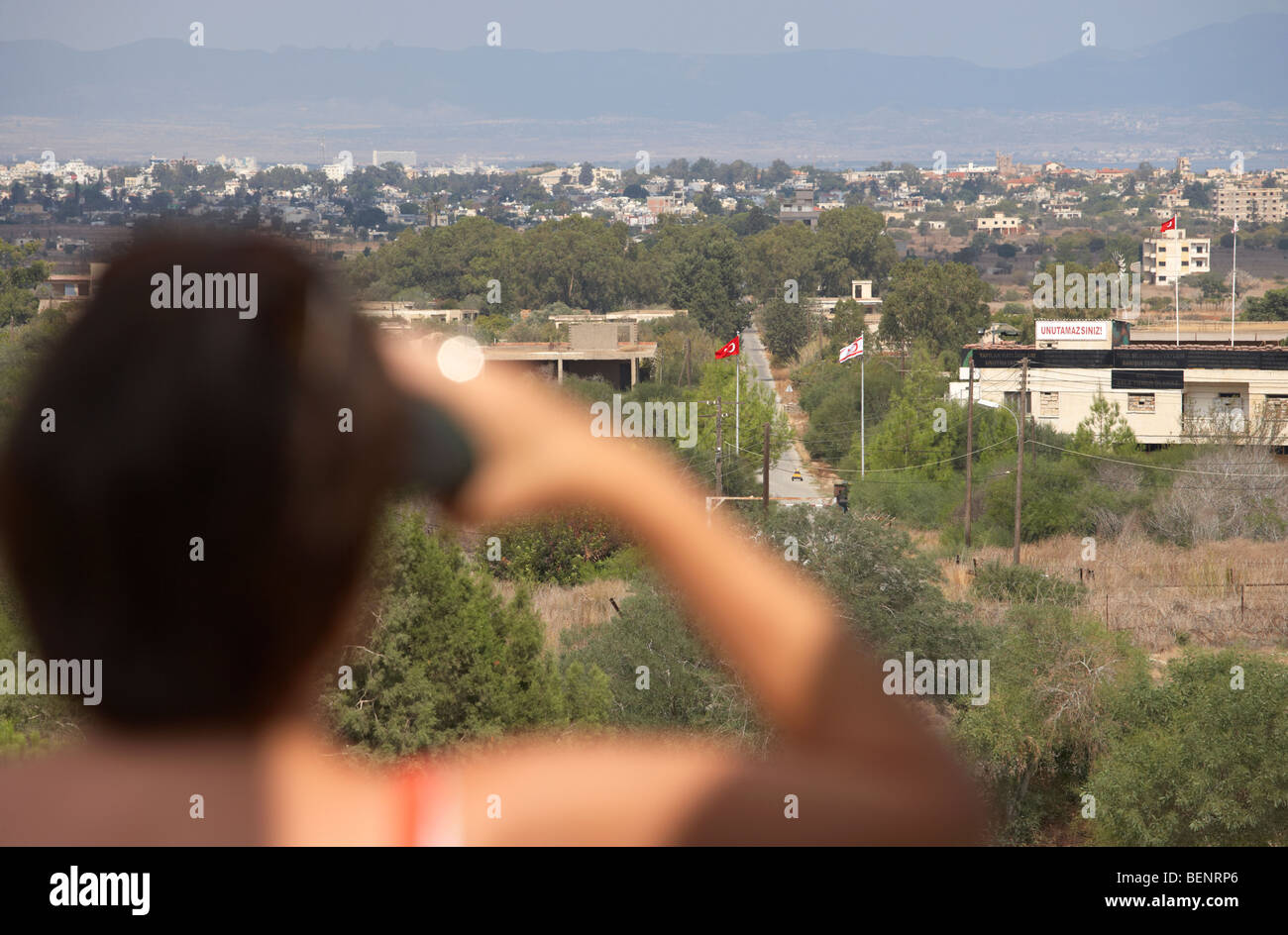 Turista femminile usando il binocolo a trascurare l'ONU zona di buffer nel verde della linea che divide il nord e il sud di Cipro a Famagosta Foto Stock