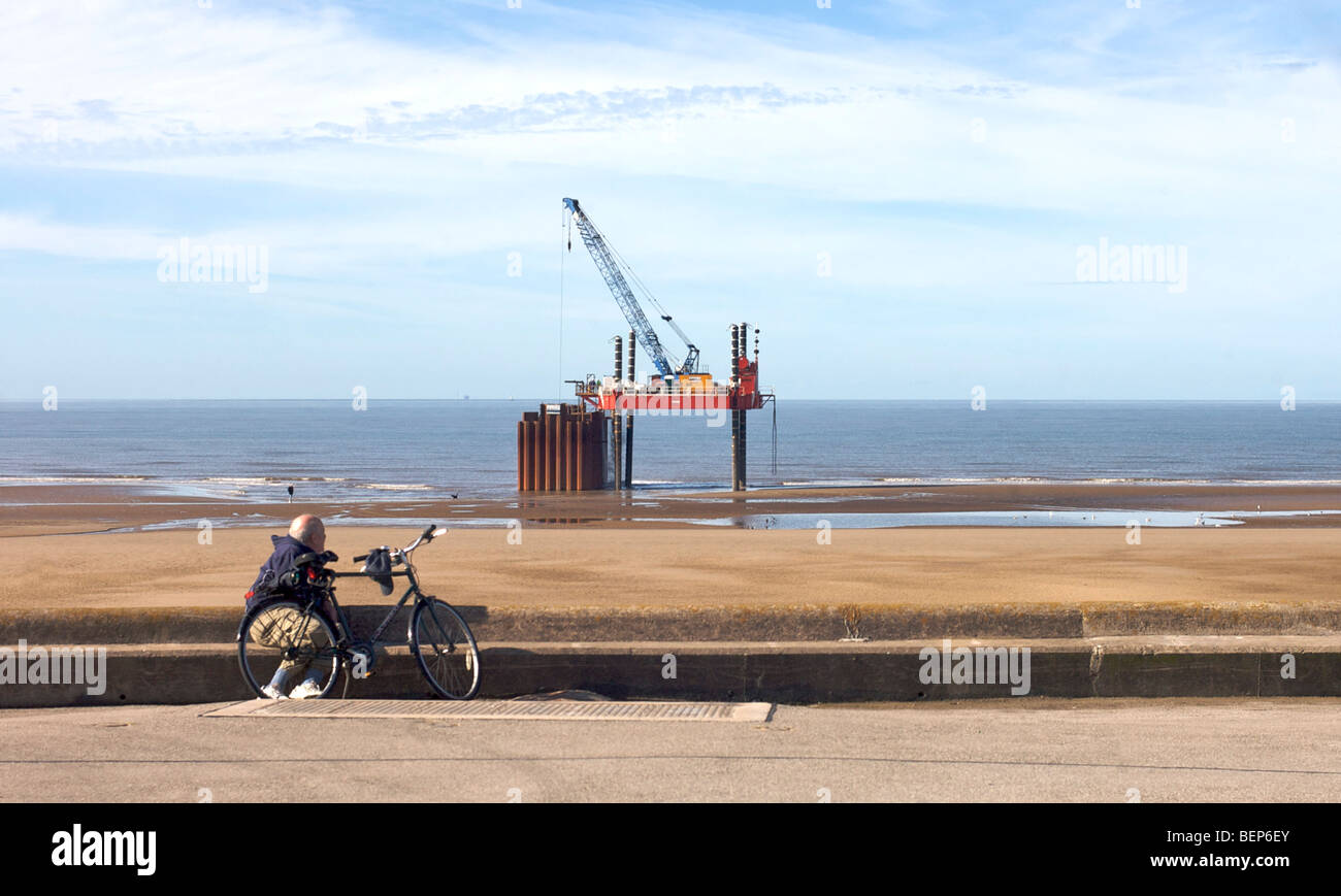 Uomo con bicicletta guardando pipeline piattaforma di riparazione sulla spiaggia Foto Stock
