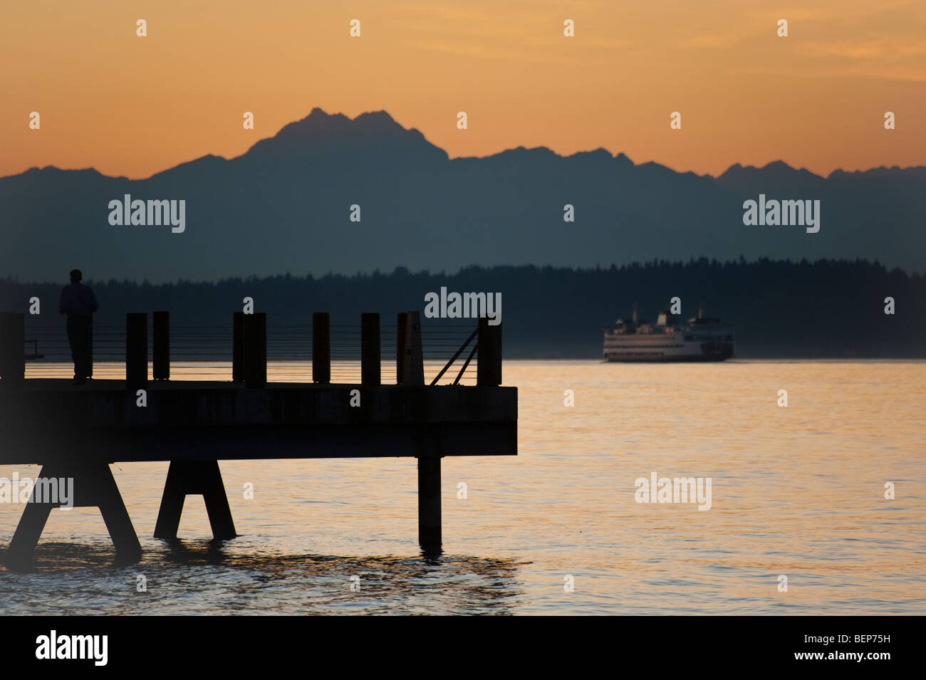 Sulla spiaggia di Alki nella zona ovest di Seattle, Washington, il sole tramonta oltre le montagne olimpiche e Bainbridge Island. Traghetto per l'isola. Foto Stock