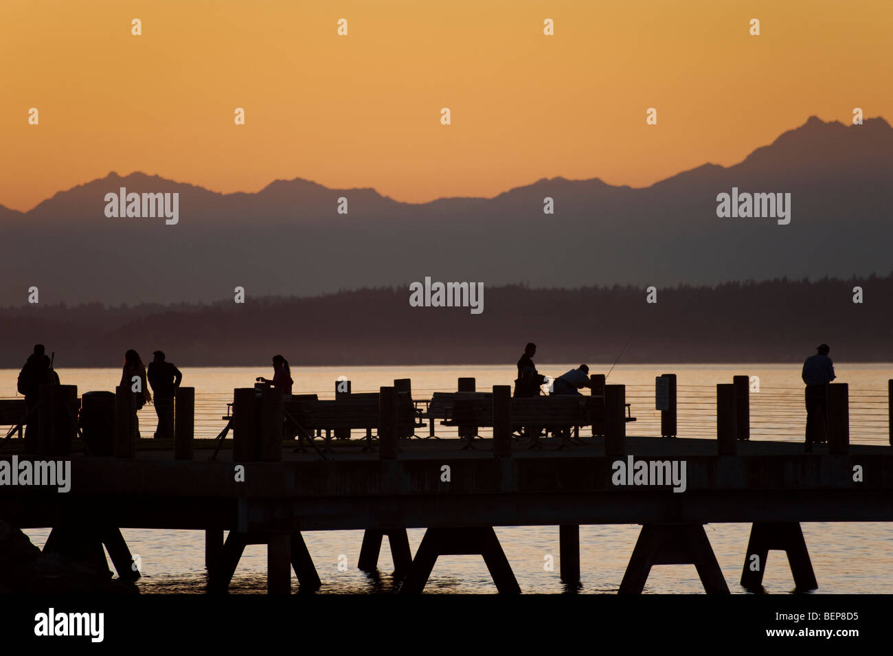 Sulla spiaggia di Alki nella zona ovest di Seattle, Washington, il sole tramonta oltre le montagne olimpiche e Bainbridge Island. Foto Stock