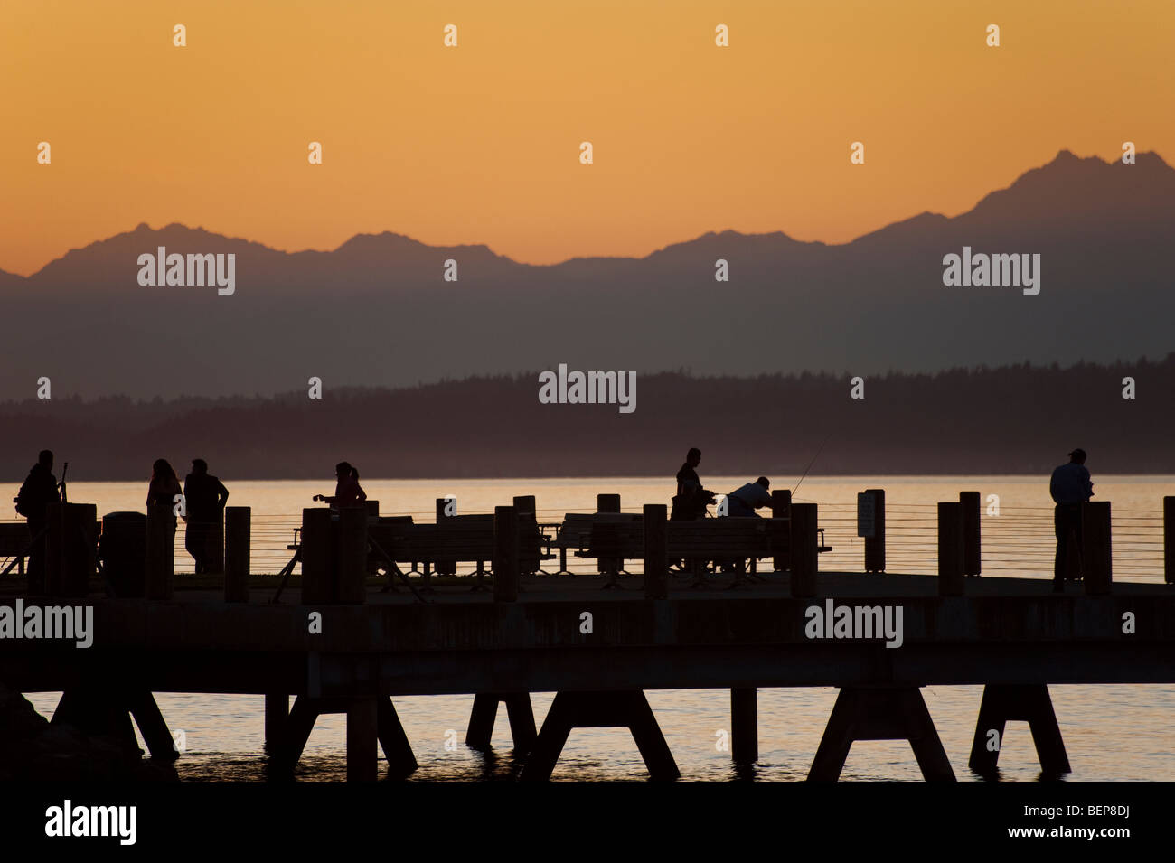 Sulla spiaggia di Alki nella zona ovest di Seattle, Washington, il sole tramonta oltre le montagne olimpiche e Bainbridge Island. Foto Stock