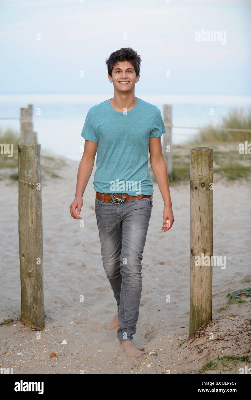 Guardando bene, bello ragazzo adolescente in piedi dal palo di legno sulla spiaggia di sabbia nel Dorset Foto Stock