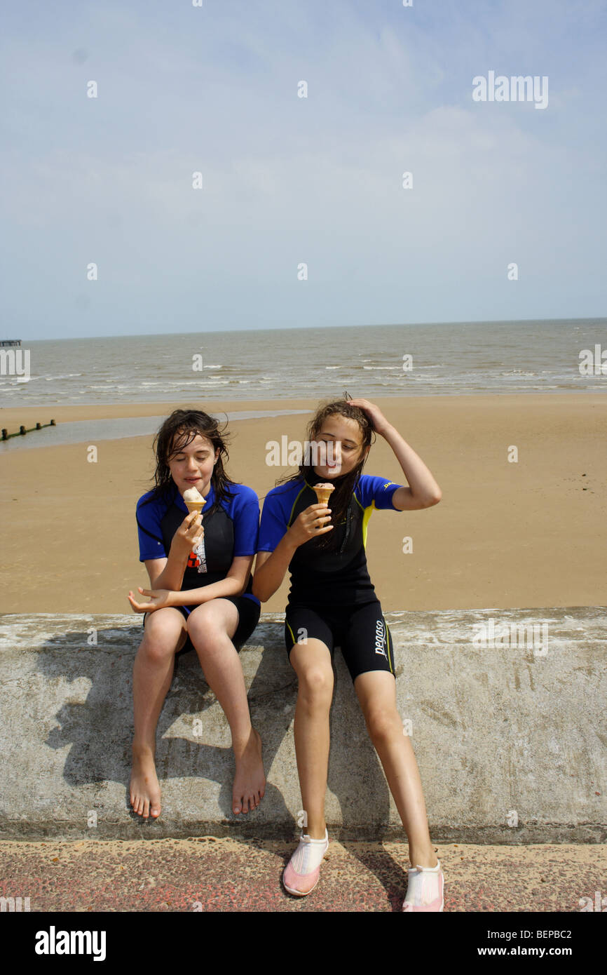 Inglese tipica località balneare di due bambini che indossano muta di mangiare gelato Foto Stock