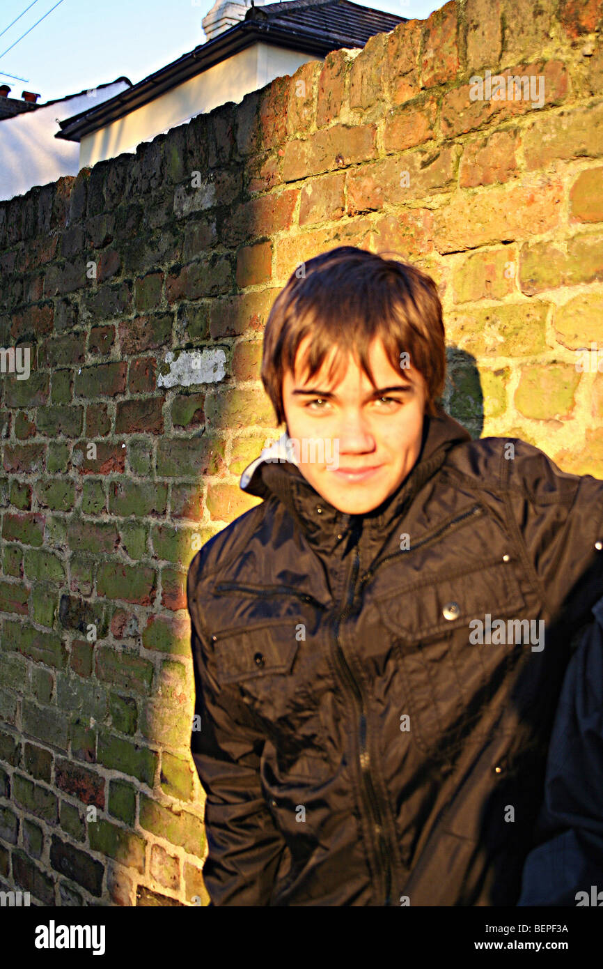 Il ragazzo si appoggia contro un muro di mattoni sorridente Foto Stock