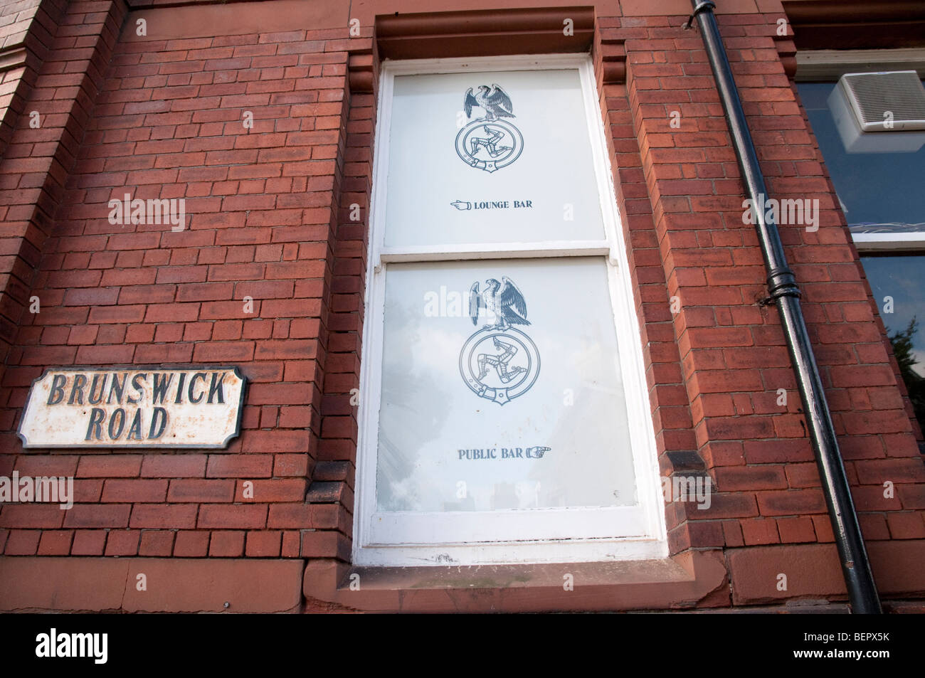 Finestra di pub che mostra isola di man su tre zampe (logo triskelion) e un vecchio cartello stradale per Brunswick Road, Douglas. Foto Stock
