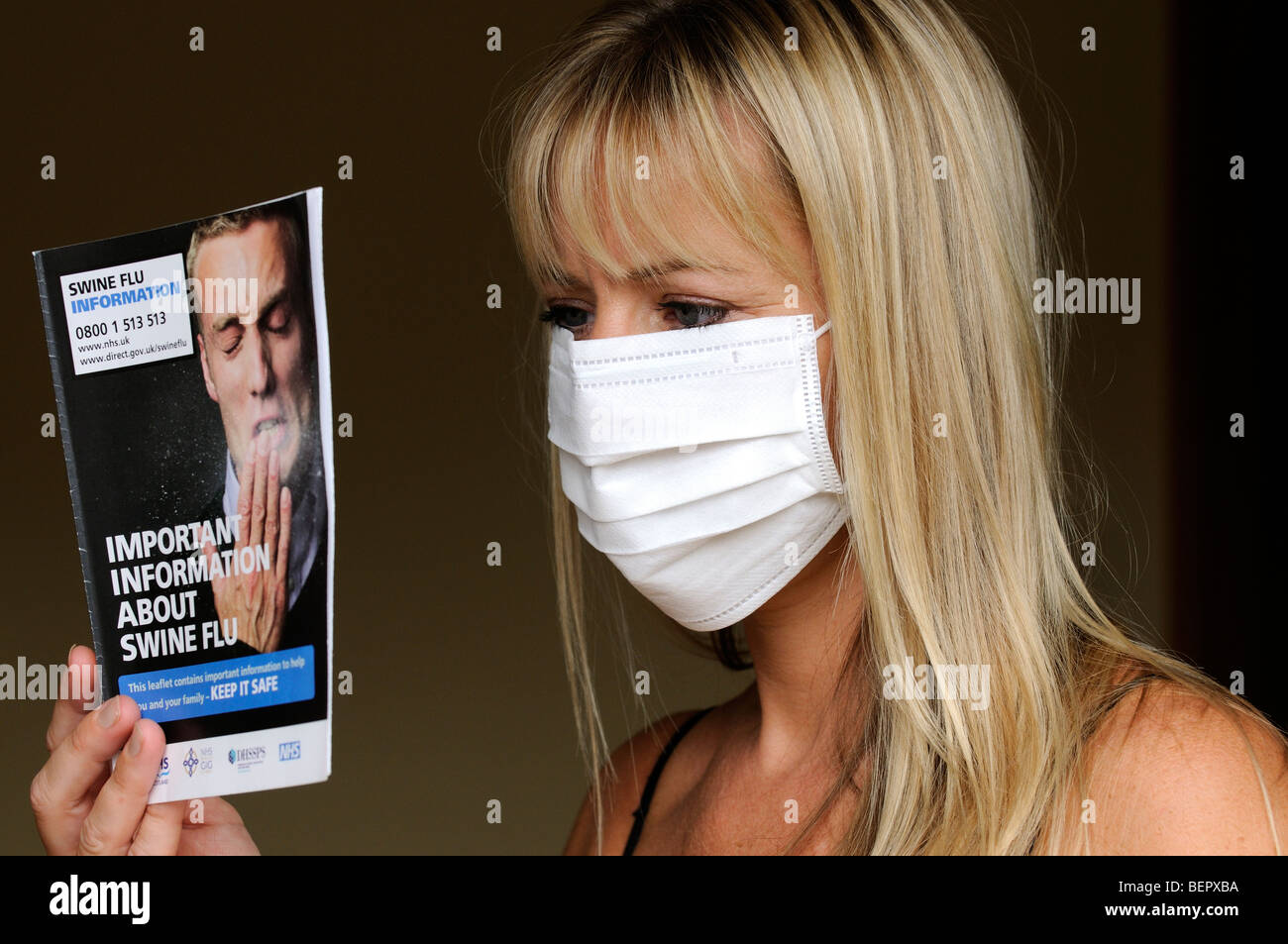 Ritratto di una donna che indossa una maschera di medici e la lettura di influenza suina opuscolo informativo Foto Stock