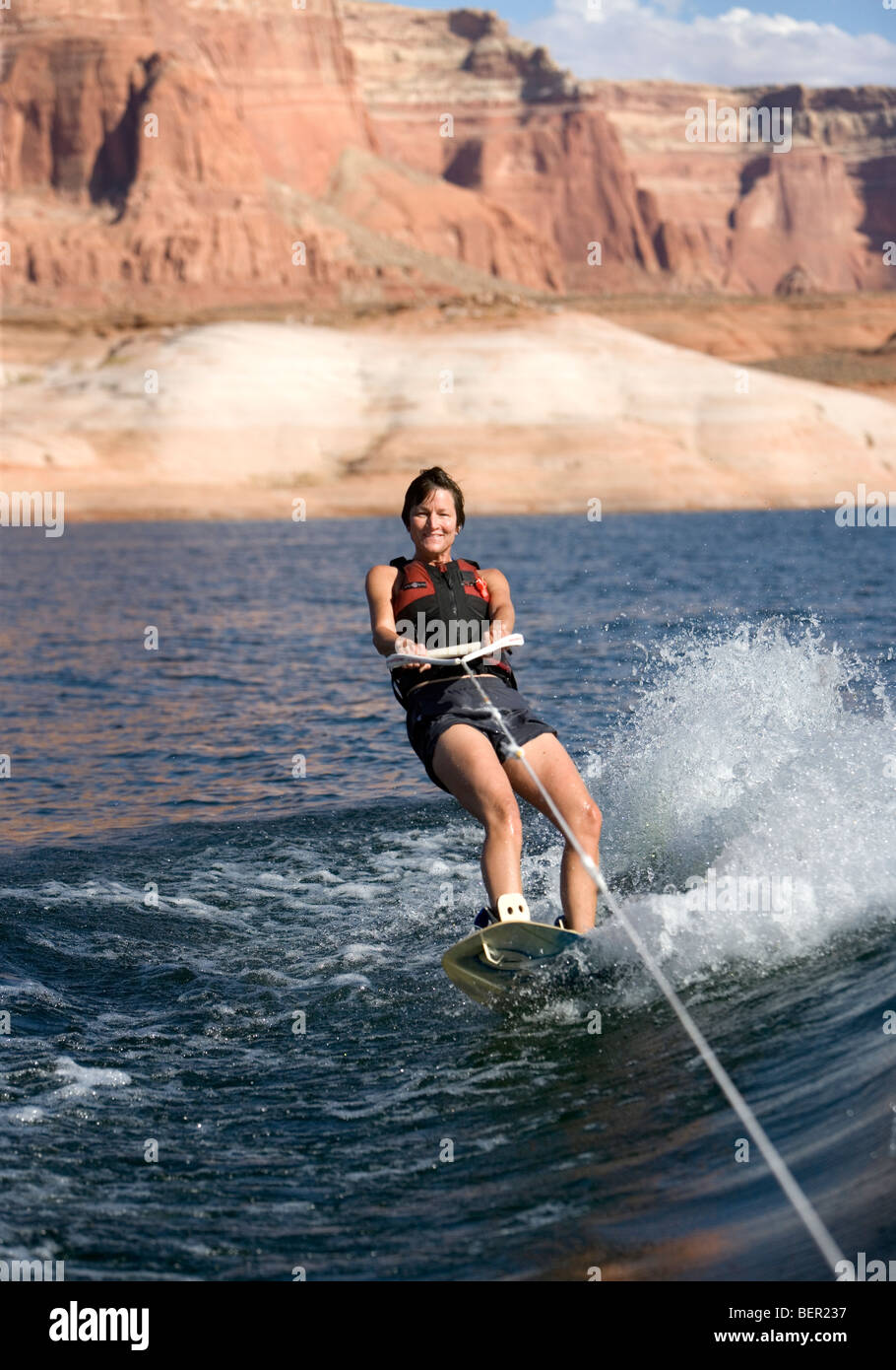 Una donna di mezza età wake boarding dietro una barca sul Lago Powel, Utah. Foto Stock