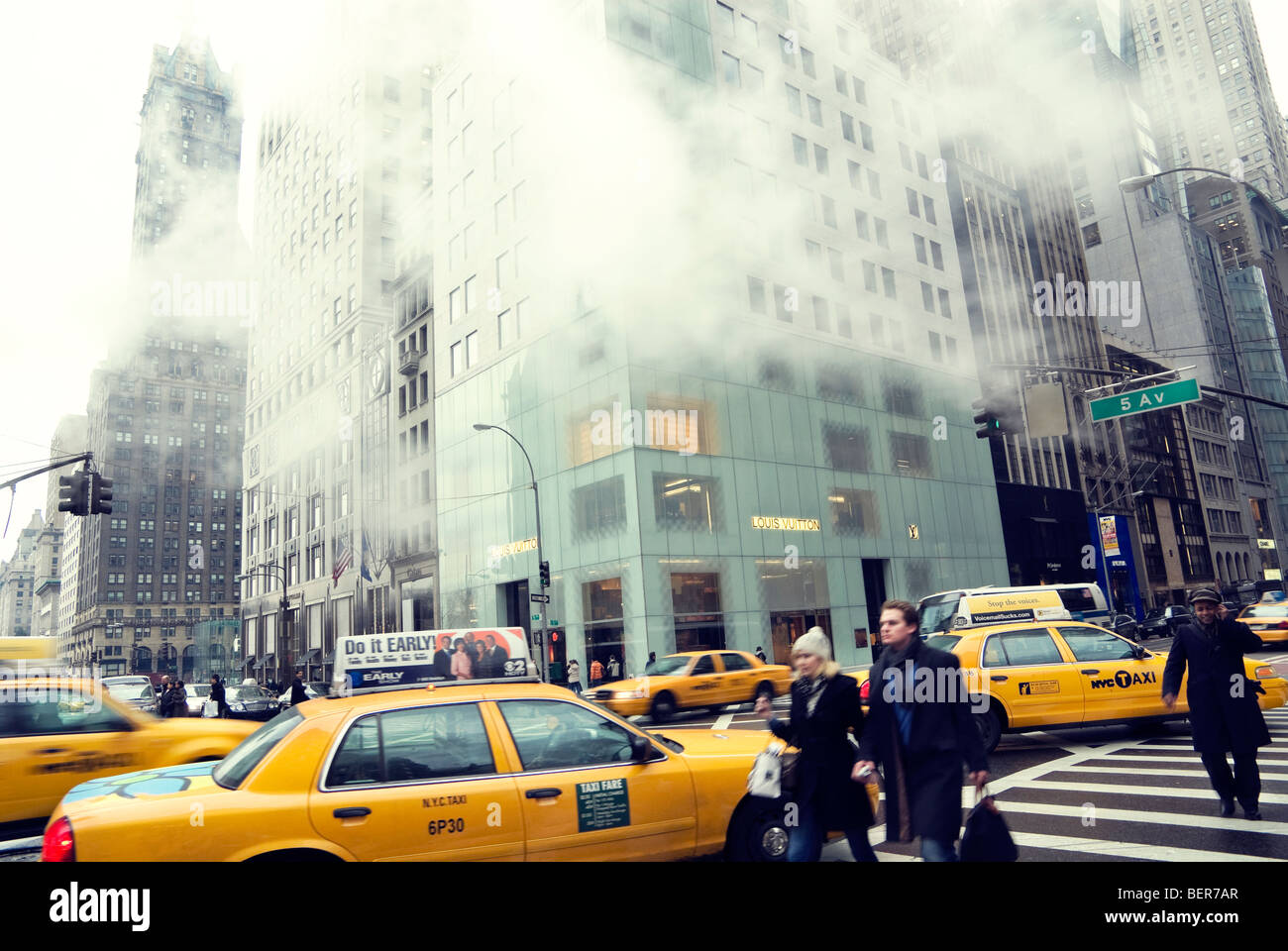 Vista invernale cercando la Quinta Avenue di New York City che dall'angolo di W 57th Street con acquirenti e taxi gialli e vapore. Foto Stock