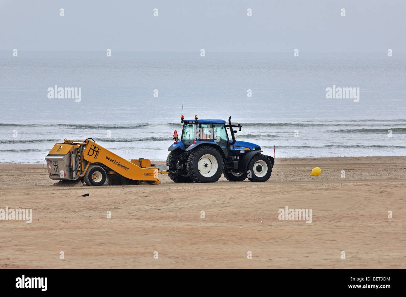 Trattore-tirato beach cleaner rastrellando sabbia di mare in località balneare lungo la costa del Mare del Nord Foto Stock