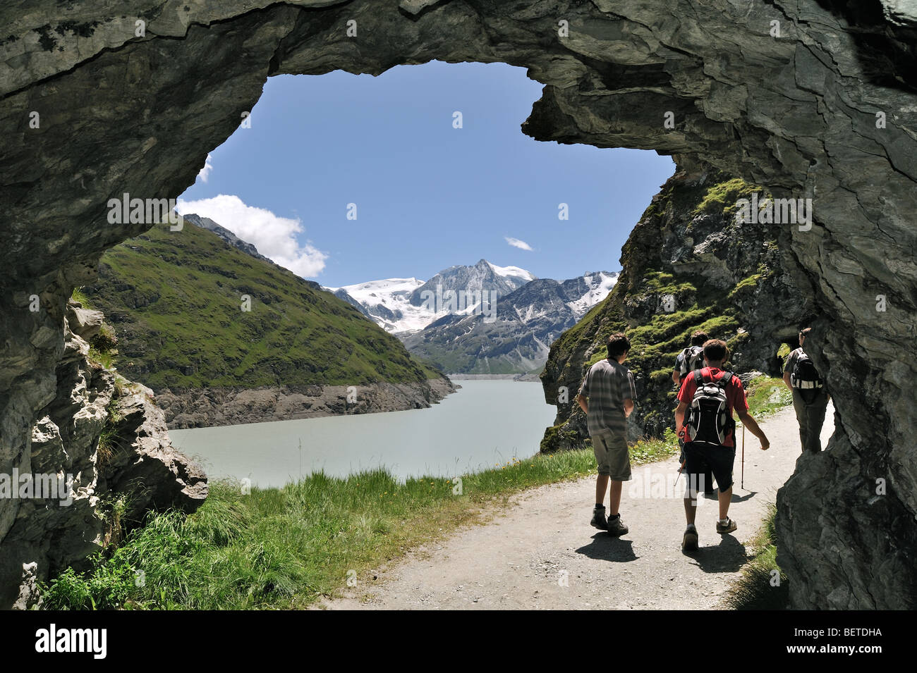 I turisti a piedi attraverso la grotta lungo il Lac des Dix, formato dalla grande diga di Dixence, Valais / Wallis, alpi svizzere, Svizzera Foto Stock