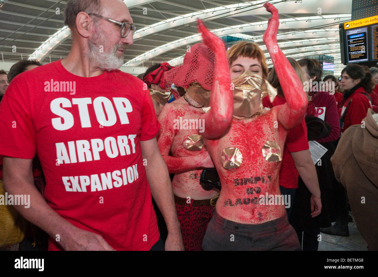 Flashmob a Heathrow Terminal 5 contro l'espansione airport & terza pista. Un led di danza da donne nel corpo la vernice dalla porta d'arte Foto Stock