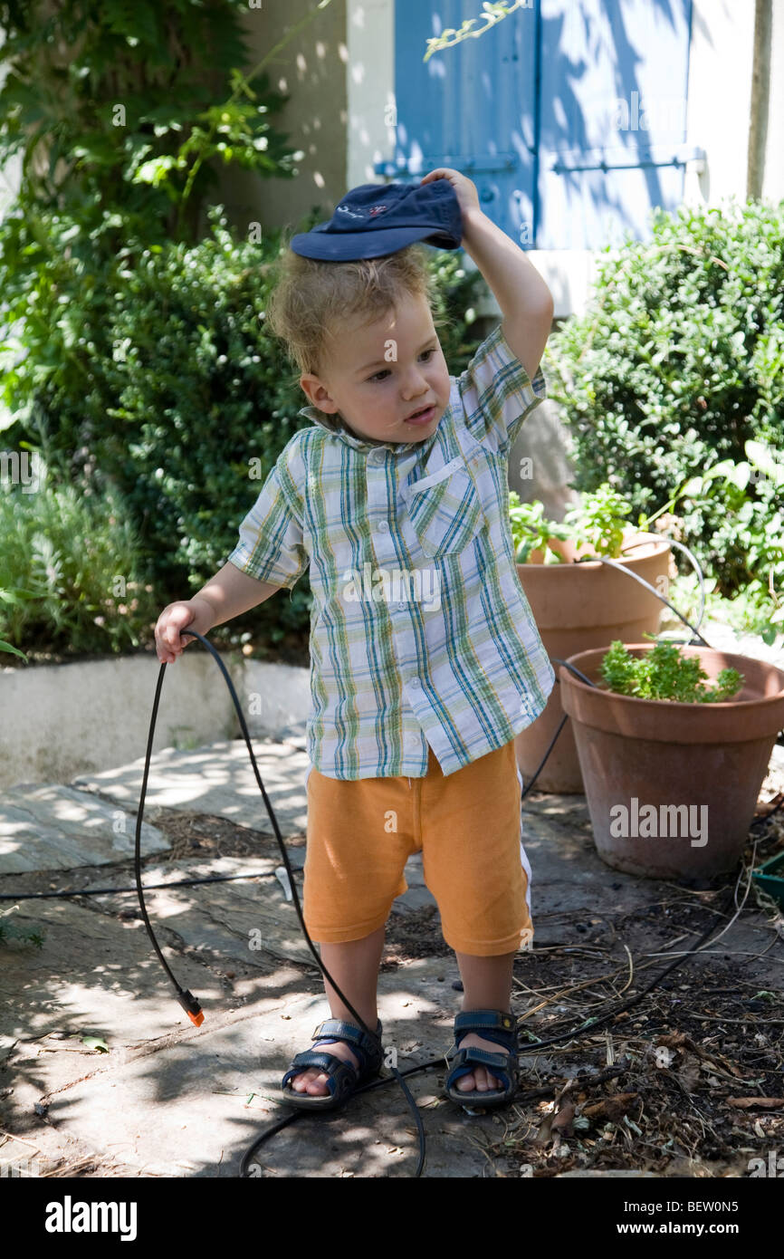 Piccolo ragazzo, bambino, umorismo, commedia, esasperazione, lottando con tubo da giardino Foto Stock