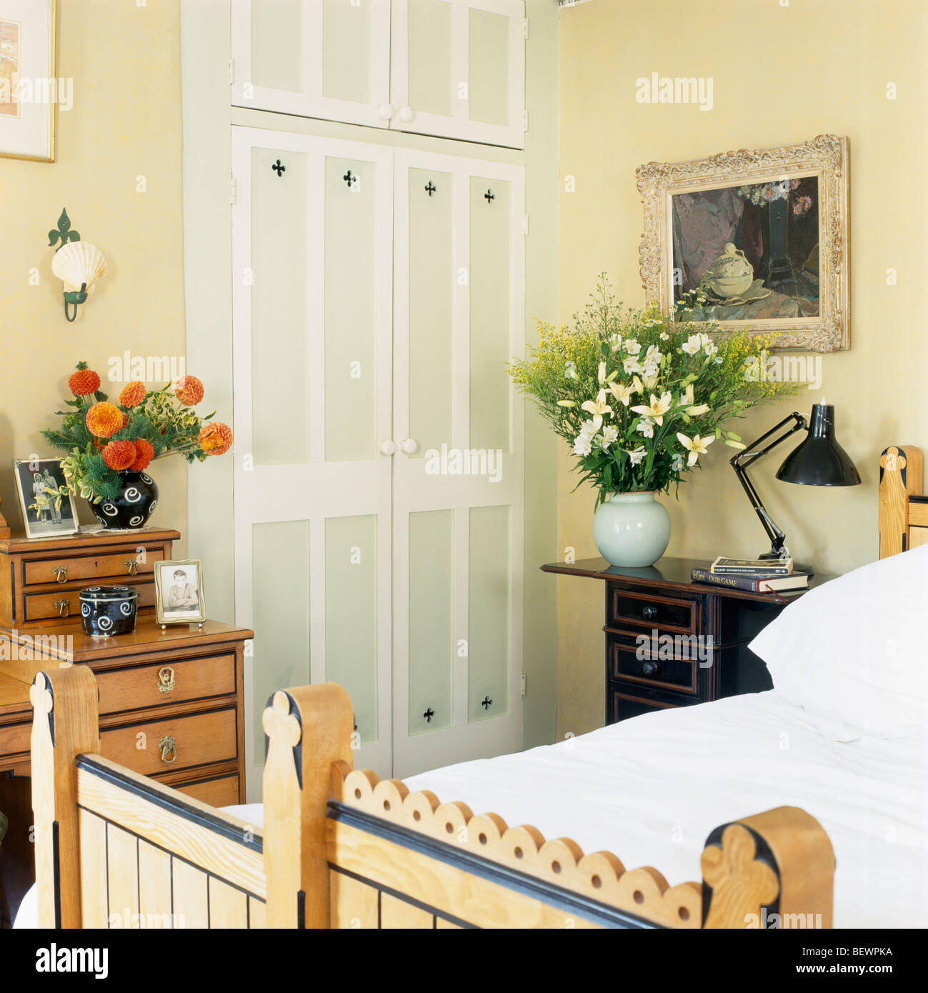 Guardaroba A Muro con porte dipinte di crema in camera da letto con foto sopra il comodino con lampada Anglepoise e vaso di fiori Foto Stock