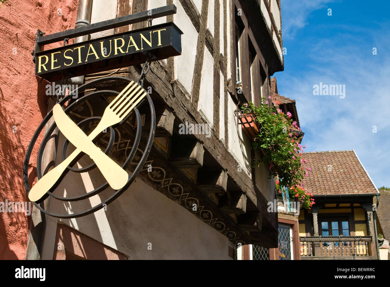 Alsazia Ristorante segno di attraversato il coltello e forchetta con tipico soleggiato Alsazia floreali case in Francia di sfondo Foto Stock