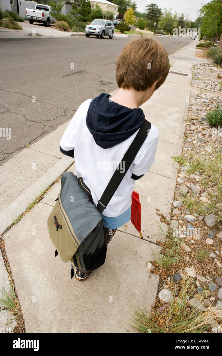 Sette anni di old boy a piedi a casa da scuola, portando la sua borsa messenger e ombrellone Foto Stock