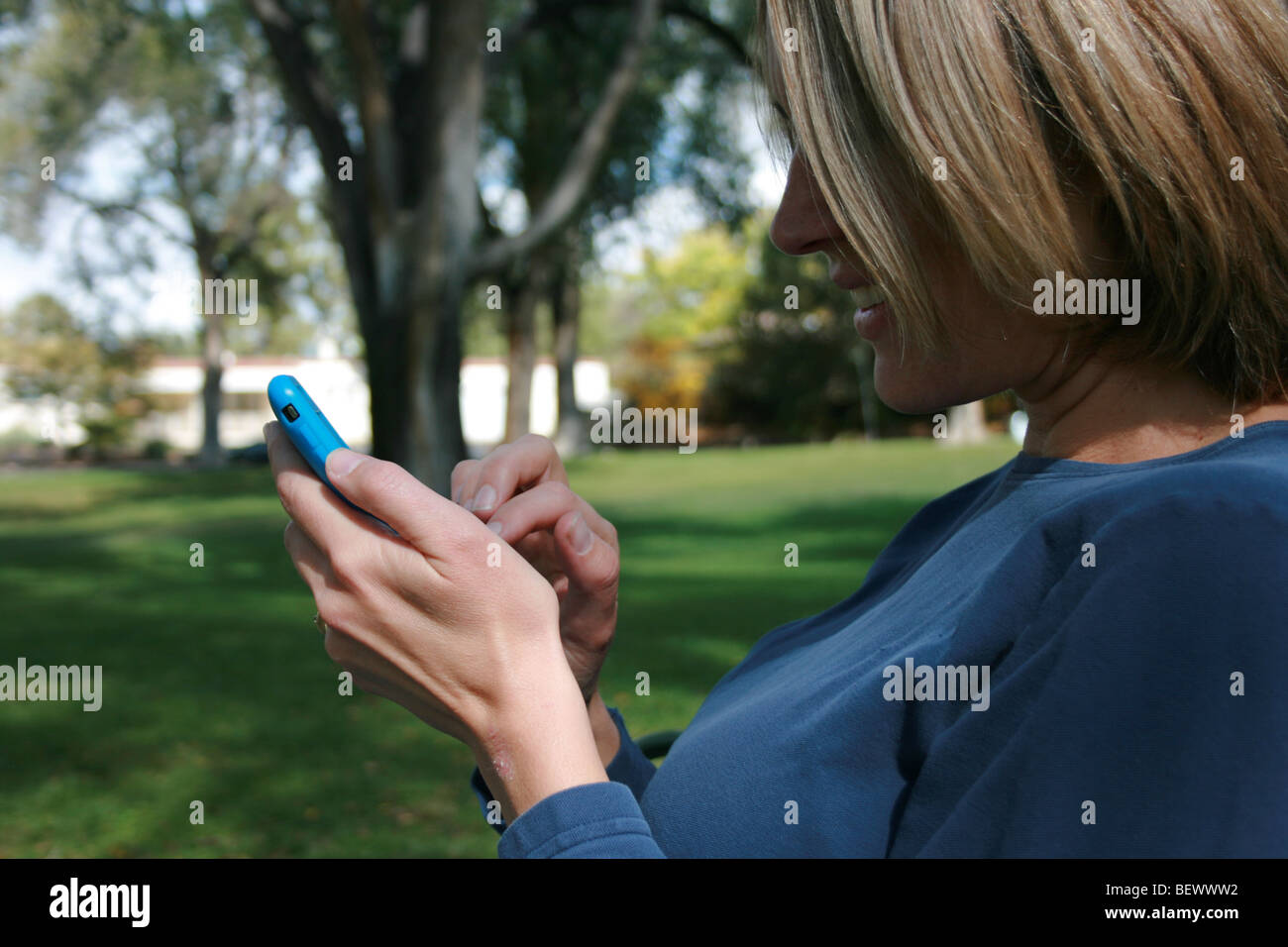 Primo piano di una donna con il suo schermo a sfioramento i-phone, seduto in un parco Foto Stock