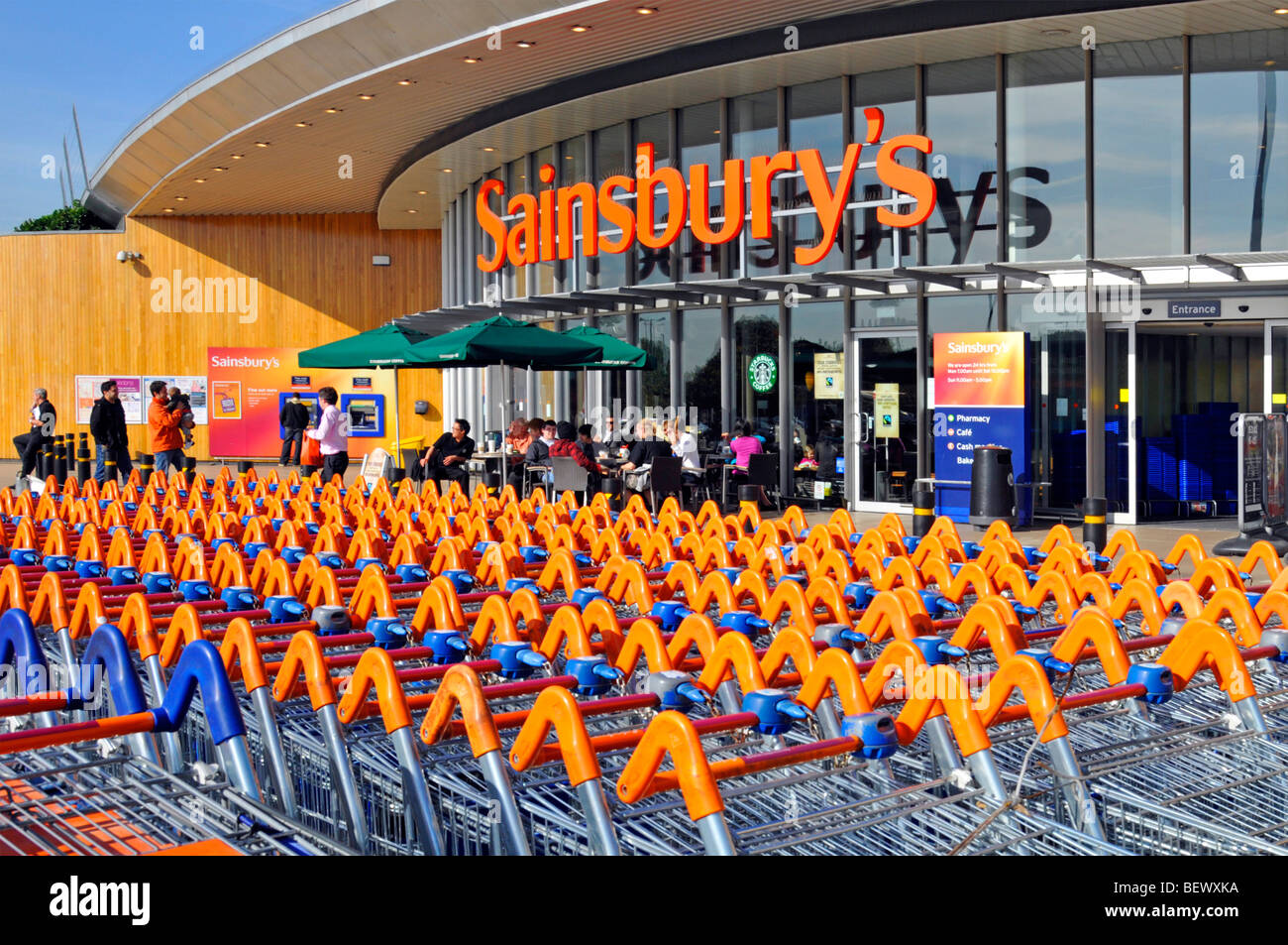 Sainsburys, supermercato, insegna e negozio, parcheggio carrello e ingresso al negozio con caffetteria Starbucks, Greenwich, Londra, Inghilterra, Regno Unito Foto Stock