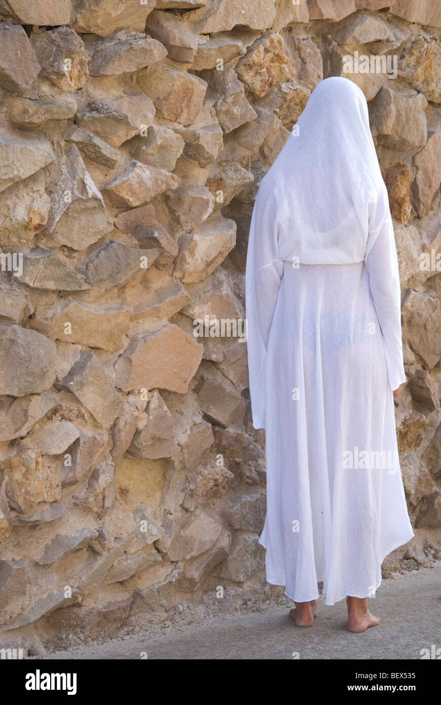 Donna su bianco sciarpa a piedi vicino al muro di pietra naturale Foto Stock