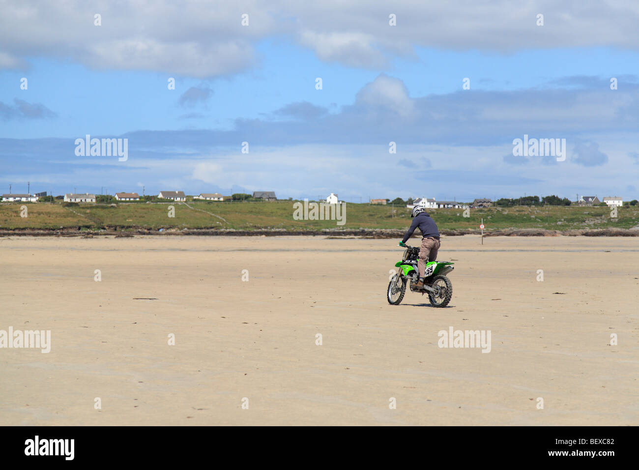 Una croce biker presso la spiaggia di sabbia sulla Omey Island con la bassa marea, Irlanda; vista Claddaghduff Foto Stock