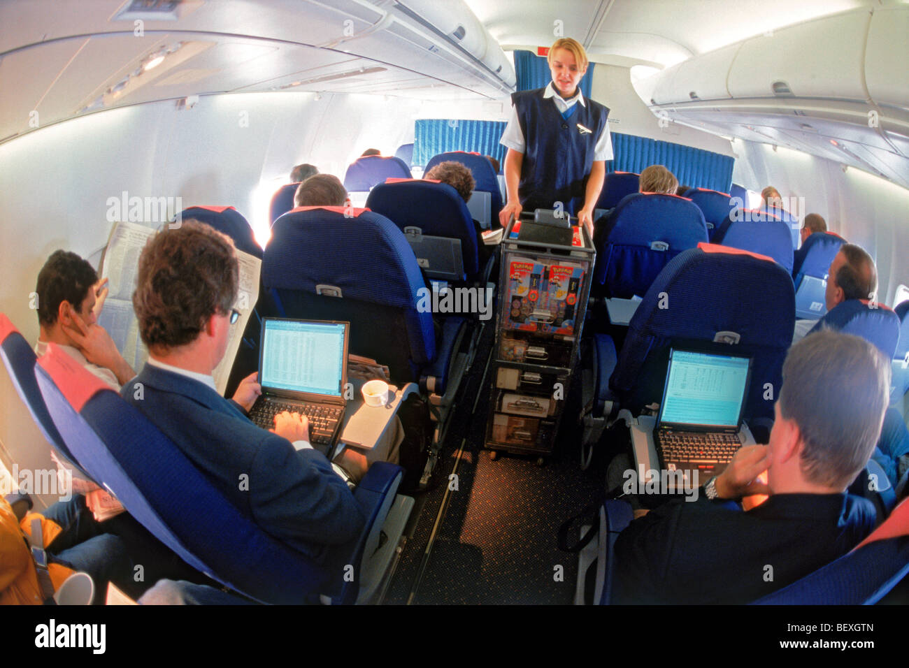 I passeggeri di aerei utilizzando computer portatili in business class con assistente di volo offre articoli duty free dal carrello Foto Stock