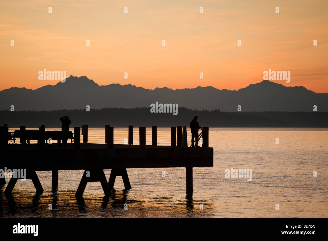Fotografo su una spiaggia di Alki Pier nella zona ovest di Seattle, Washington. Il sole tramonta oltre le montagne olimpiche e Bainbridge Island. Foto Stock