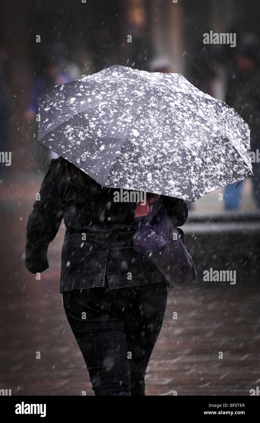 Una donna che ospita dalla neve pesante come lei cammina giù Buchanan Street, Glasgow, Scozia. Foto Stock