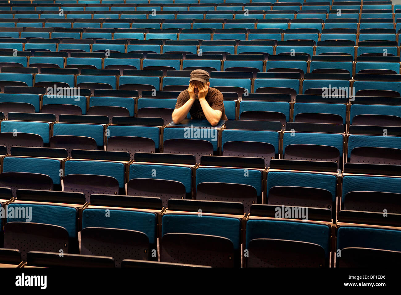 Un uomo seduto in un auditorium, mani che coprono gli occhi Foto Stock