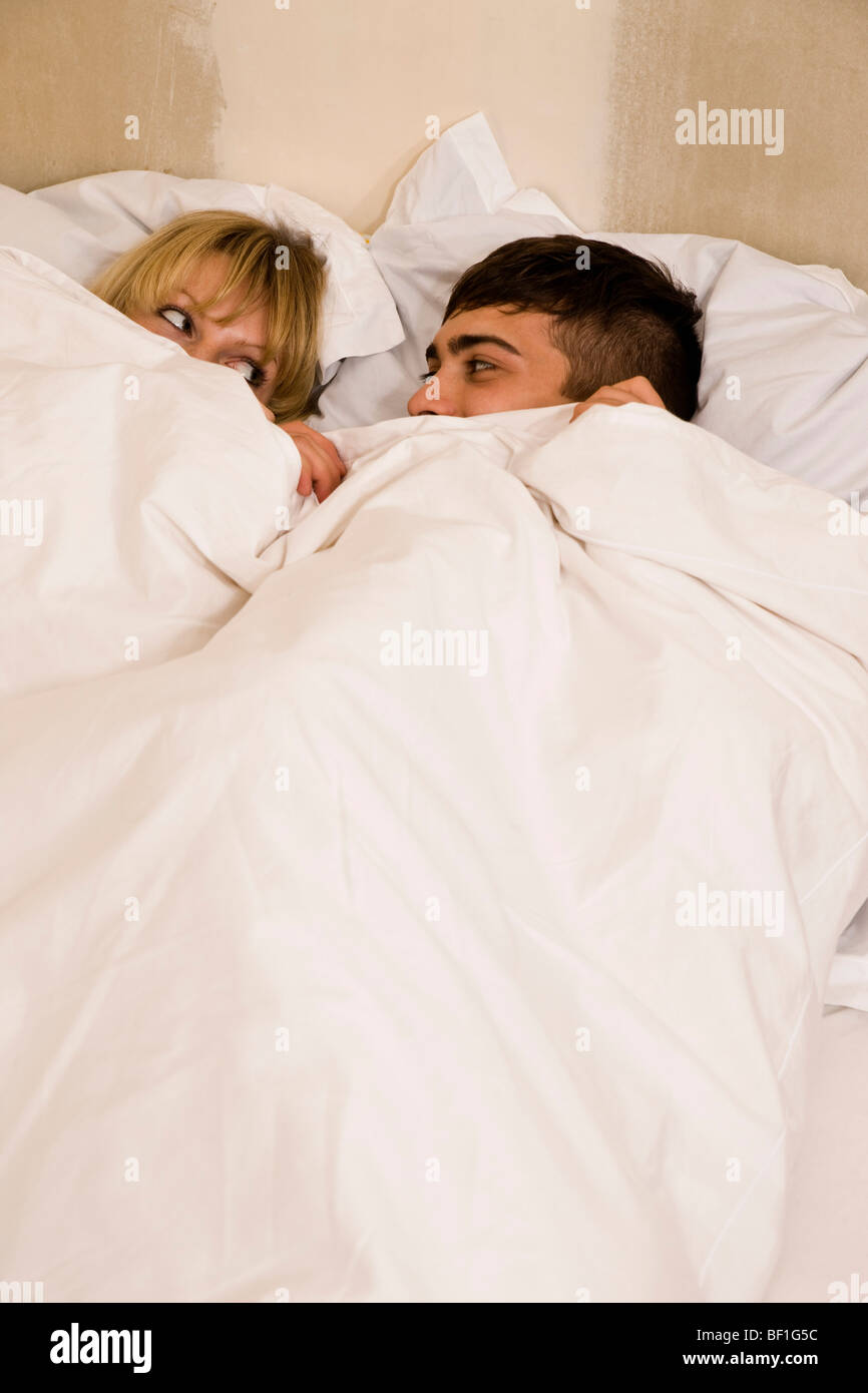 Una giovane coppia in letto con il piumone tirato fino ai loro occhi Foto Stock