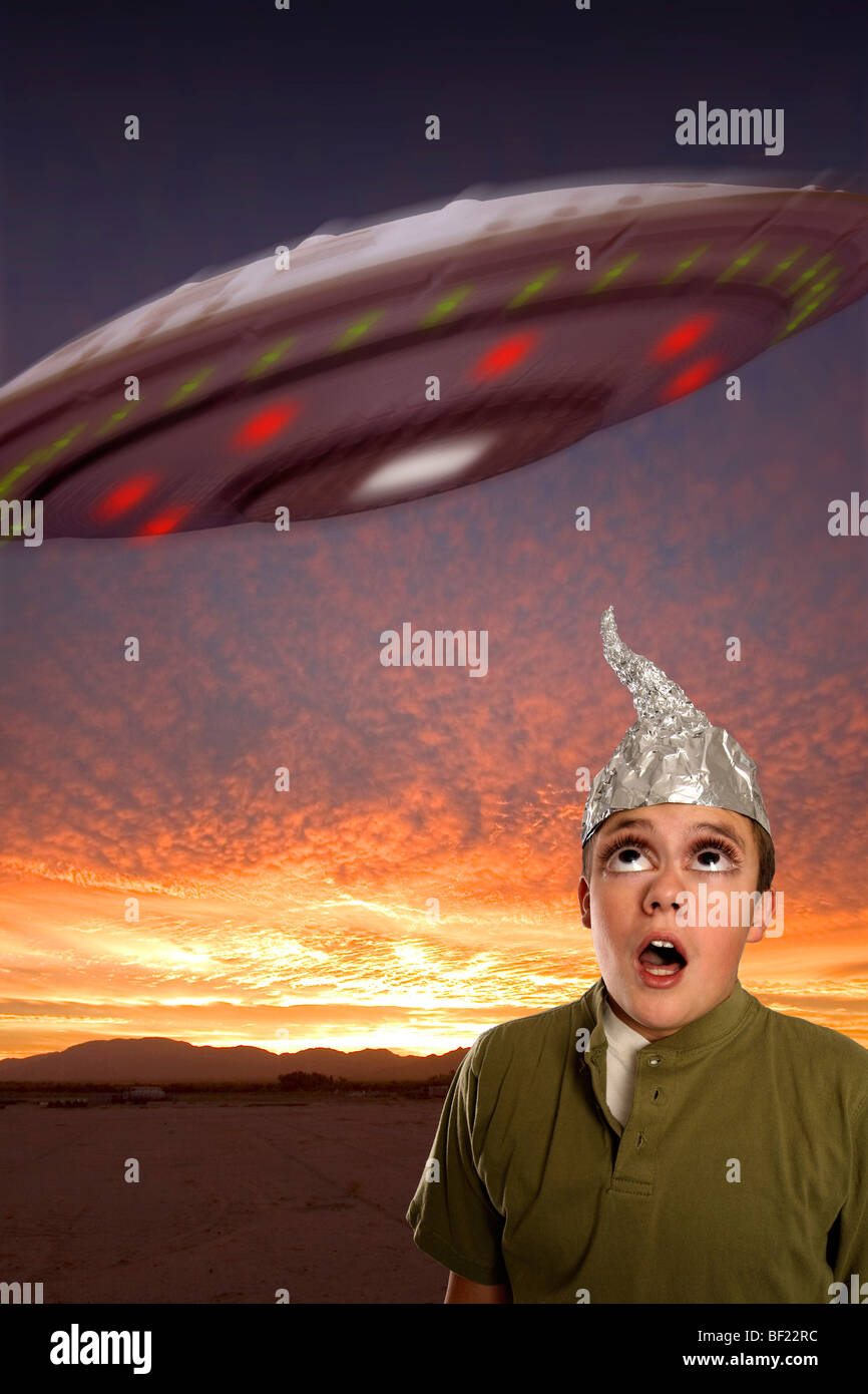 Un bug-eyed boy, indossando un stagno-foil hat osserva un UFO nel cielo. Foto Stock