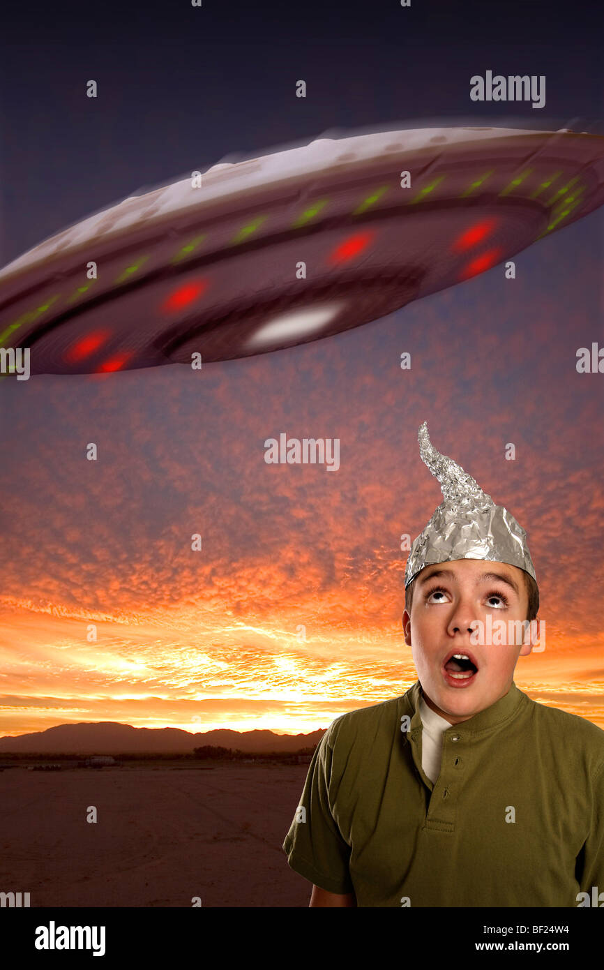 Un ragazzo che indossa un stagno-foil hat osserva un UFO nel cielo. Foto Stock