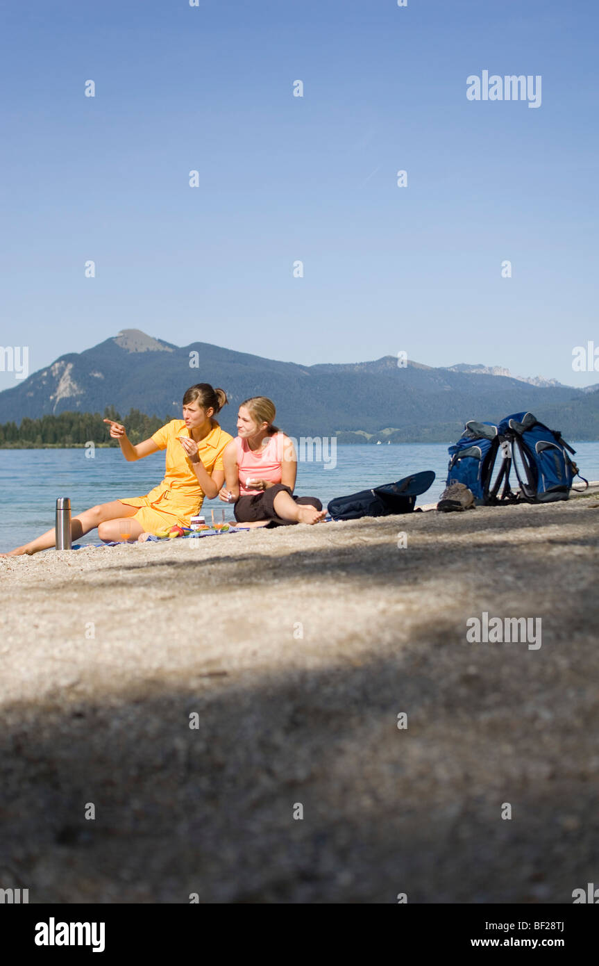 Due giovani donne e ragazze, avente un picnic in riva al lago, il Lago Walchensee, Alta Baviera, Baviera, Germania Foto Stock