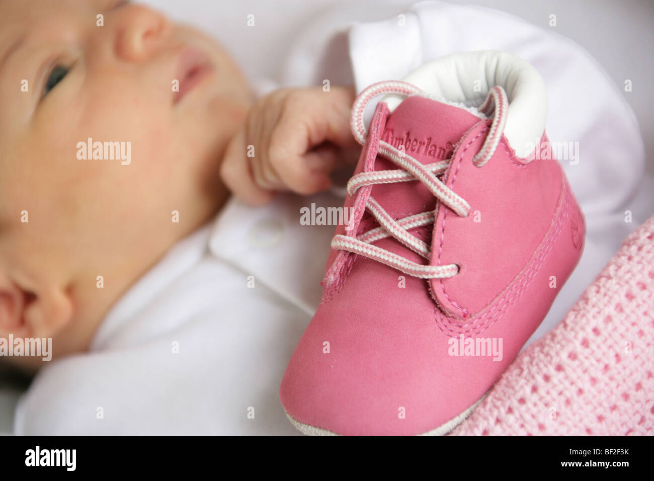 Neonati prime scarpe con un molto giovane bambina fuori fuoco in background. Foto Stock