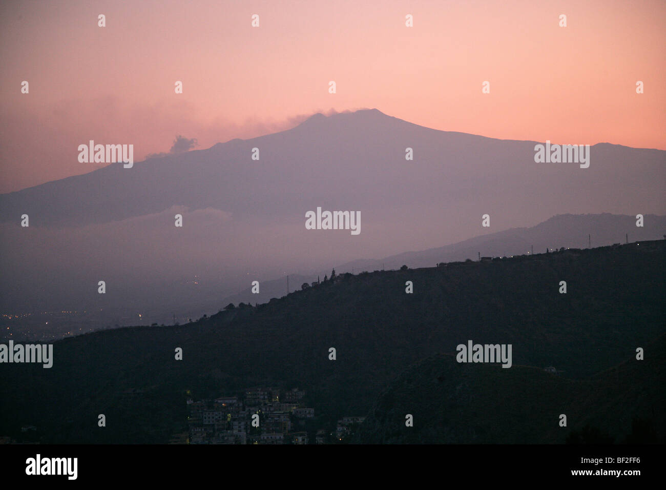 Il vulcano attivo dell'Etna fuma come il crepuscolo scende oltre la città di Taormina in Sicilia in Italia Foto Stock