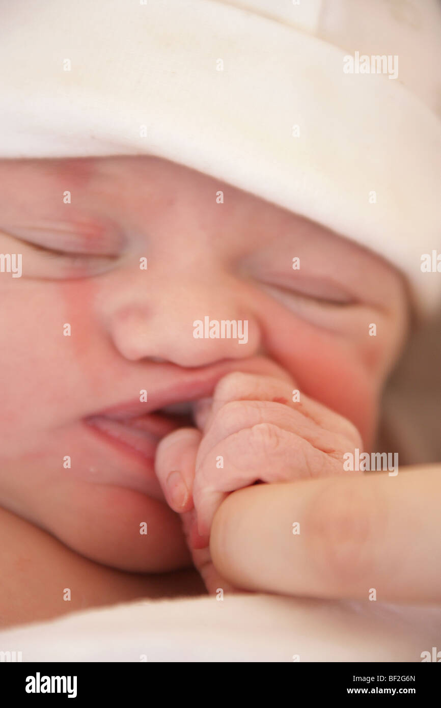 Ritratto di un neonato ragazza avvolto in una coperta e addormentato veloce trattenendo il suo dito di madri, poche ore dopo la nascita. Foto Stock